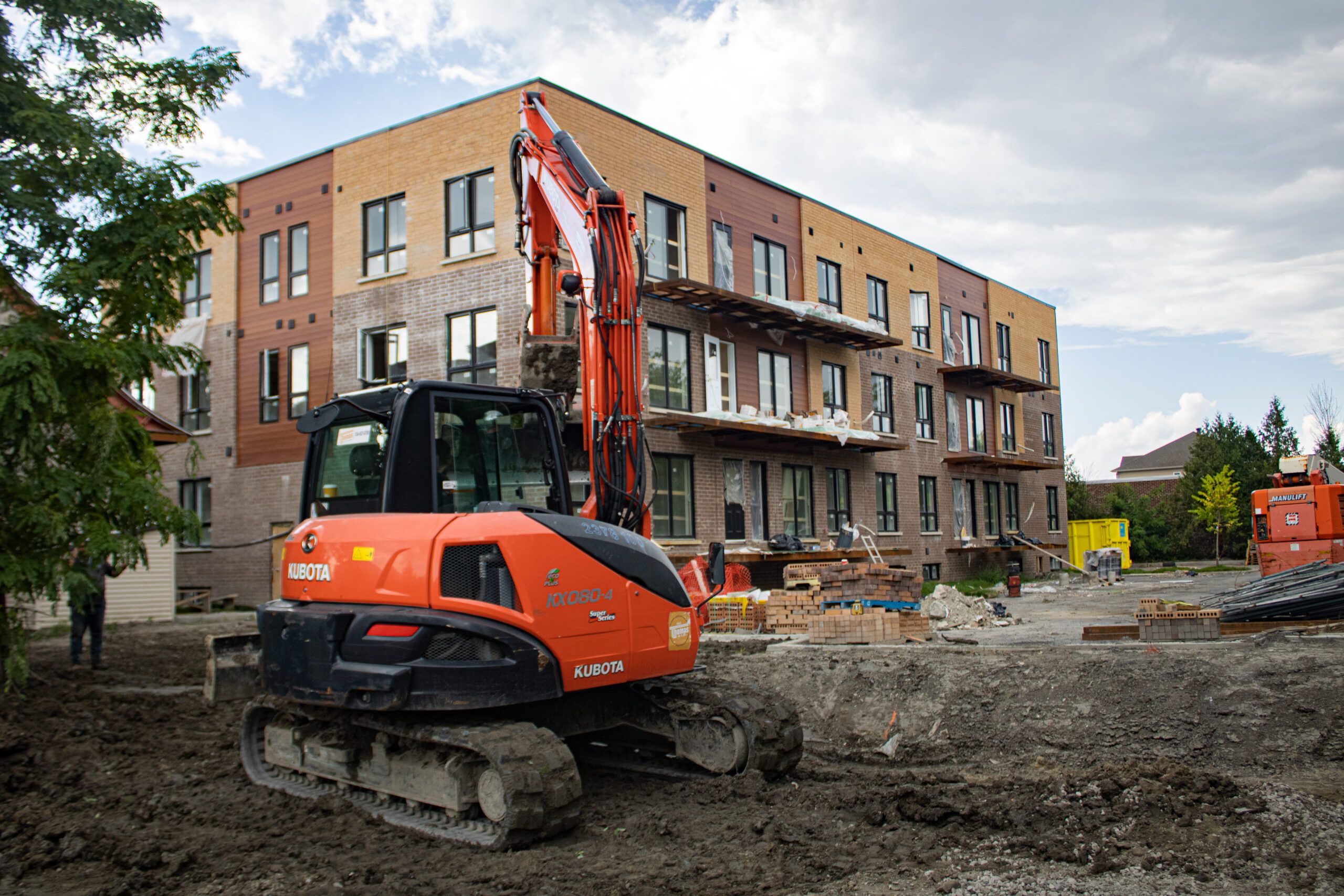 A Kubota mini excavator on a construction site in front of a multi-family building under construction, representing excavation services in Quebec, commonly used for digging and earthmoving tasks in residential projects.