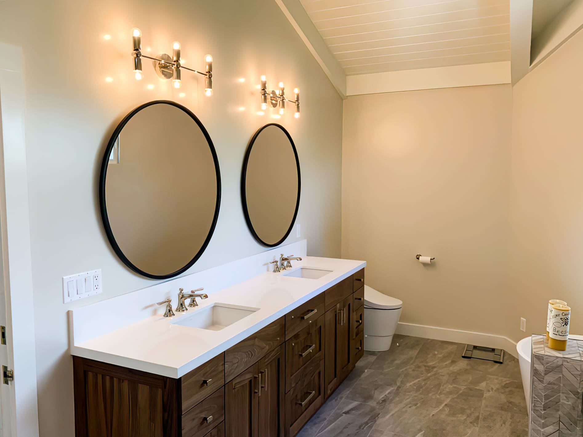 Modern bathroom with double vanity featuring white countertop, wooden drawers, oval mirrors with black frames, and marble-look tile floor, representing elegant bathroom design and remodeling in Quebec.