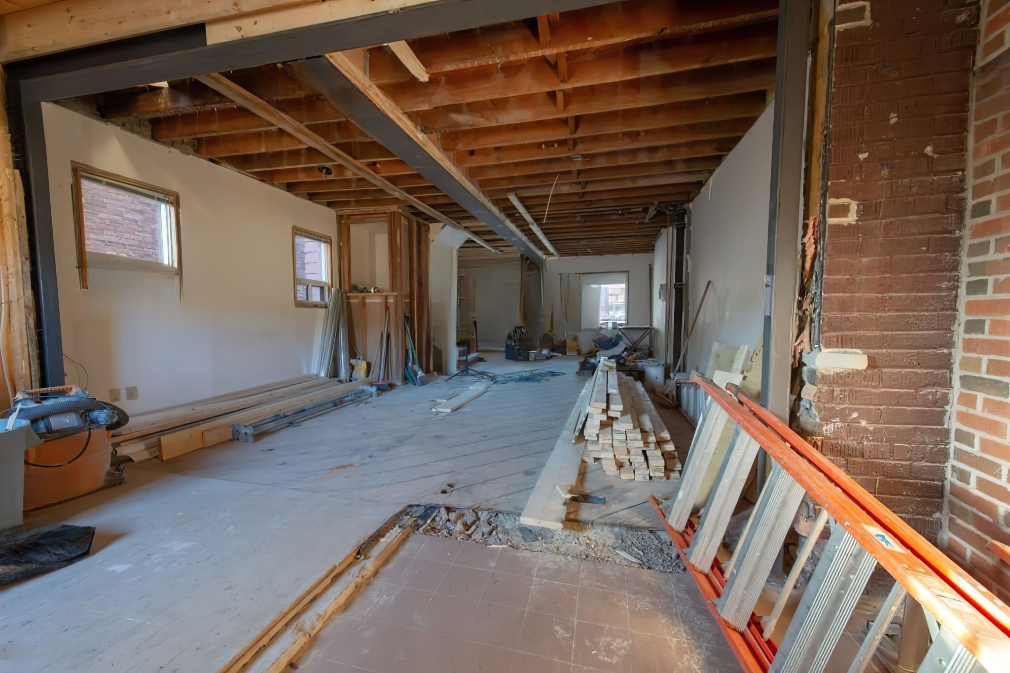 An interior of a building in Quebec during renovation, showing exposed ceiling beams, a large steel support beam, unfinished walls, and construction materials, representing Structural Modification Services Quebec.