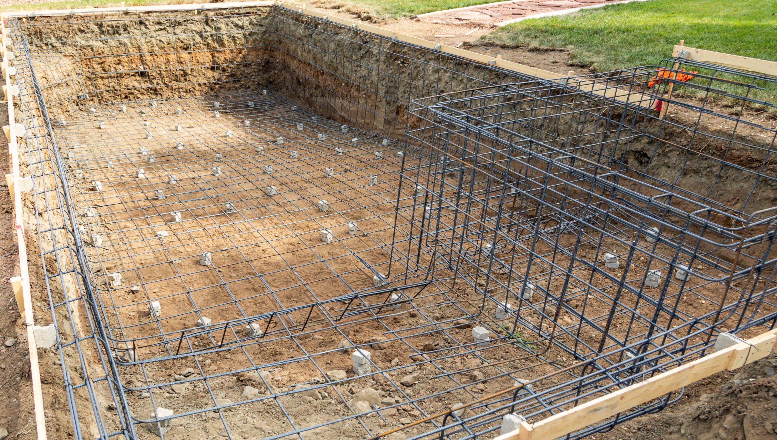 A construction site showing the excavation for a concrete swimming pool, prepared for pouring the base and walls with reinforced concrete.