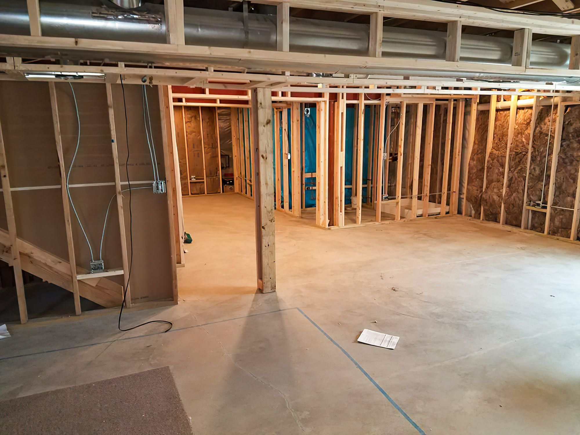 A basement under construction in Quebec with concrete flooring, wooden framing, visible insulation, and exposed wiring and plumbing — showing preparation for basement finishing and interior installation.