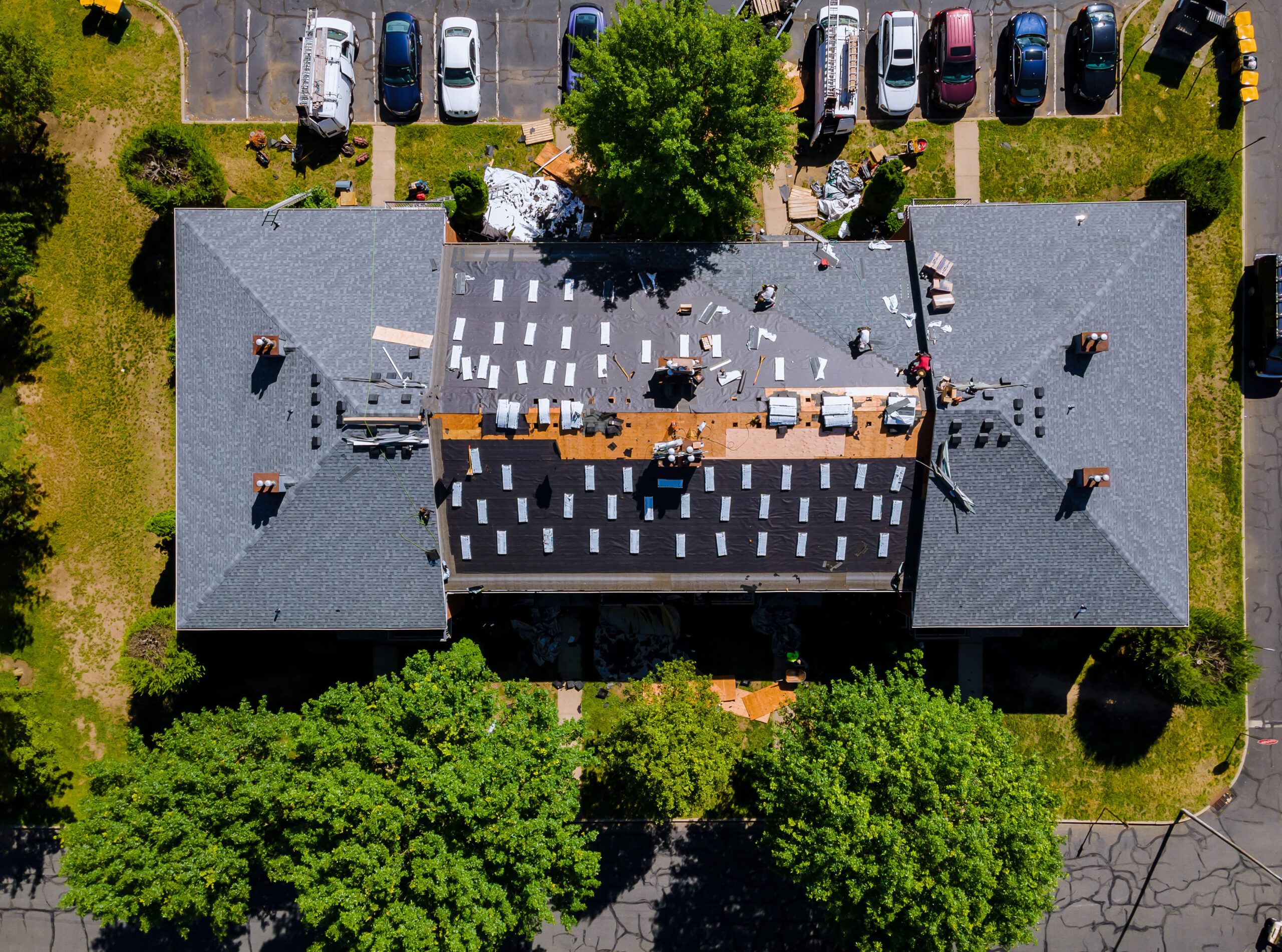 Roof installation in Montreal showing an aerial view of a building where workers are repairing or replacing the roof, with new roofing materials installed on most of the surface and old debris piles visible among construction equipment and materials.