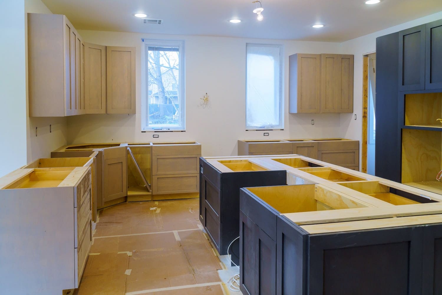 Kitchen under renovation with bright upper cabinets, dark lower cabinets, and an unfinished island awaiting hardware installation, showcasing detailed craftsmanship in kitchen design and remodeling in Quebec.