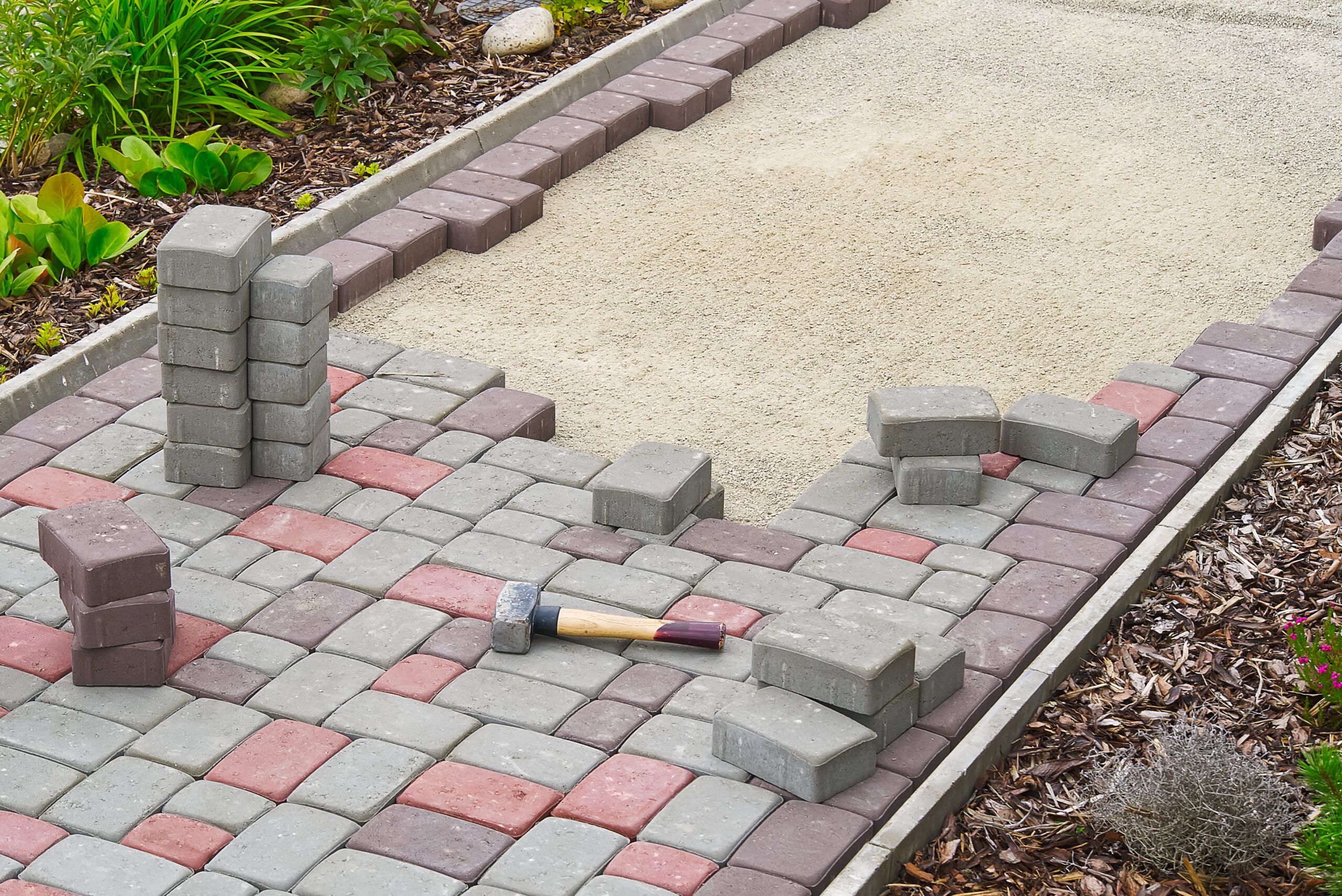 Construction of a stone walkway showing gravel base, edge stones, and paving stones being laid in a pattern — representing professional landscaping and paving services in Quebec.