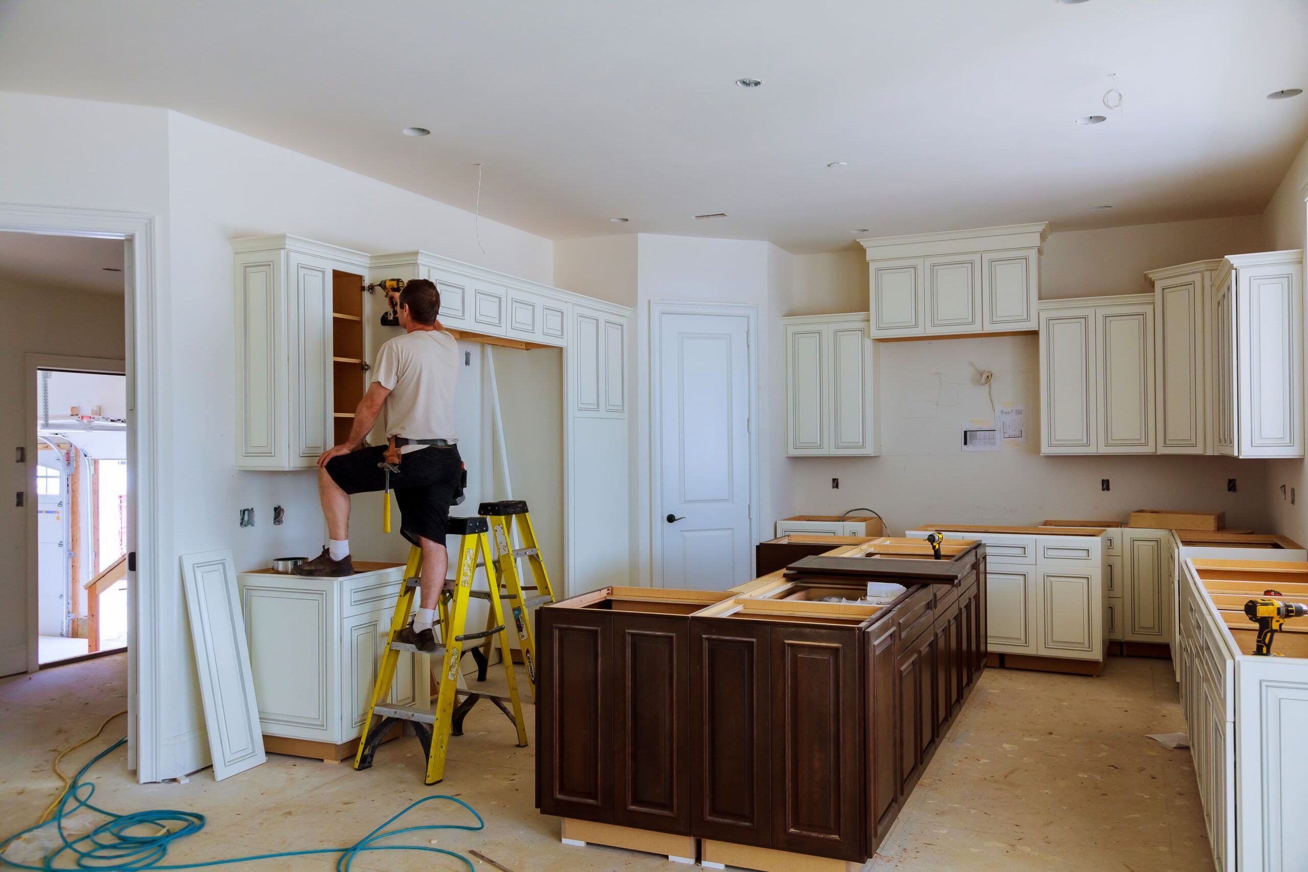 Contractor installing cream-colored kitchen cabinets during a home renovation, with a dark wood island in progress, representing professional kitchen design and remodeling in Quebec for modern homes.