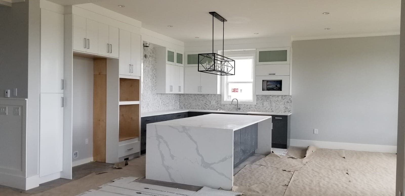 Kitchen under construction featuring a marble-look quartz island, white and dark gray cabinets, and modern pendant lighting, showcasing elegant kitchen design and remodeling in Quebec.