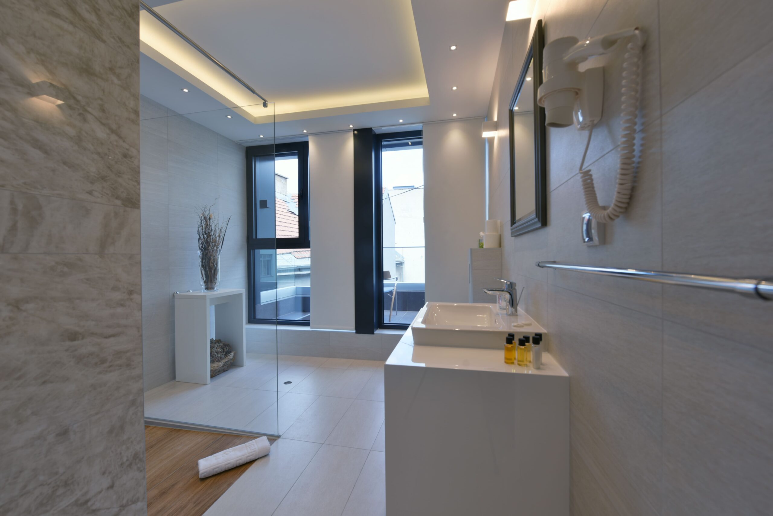 Modern bathroom with glass shower, sink, and wall-mounted hair dryer, featuring large ceramic tiles and bright lighting that reflect contemporary bathroom design and remodeling in Quebec.