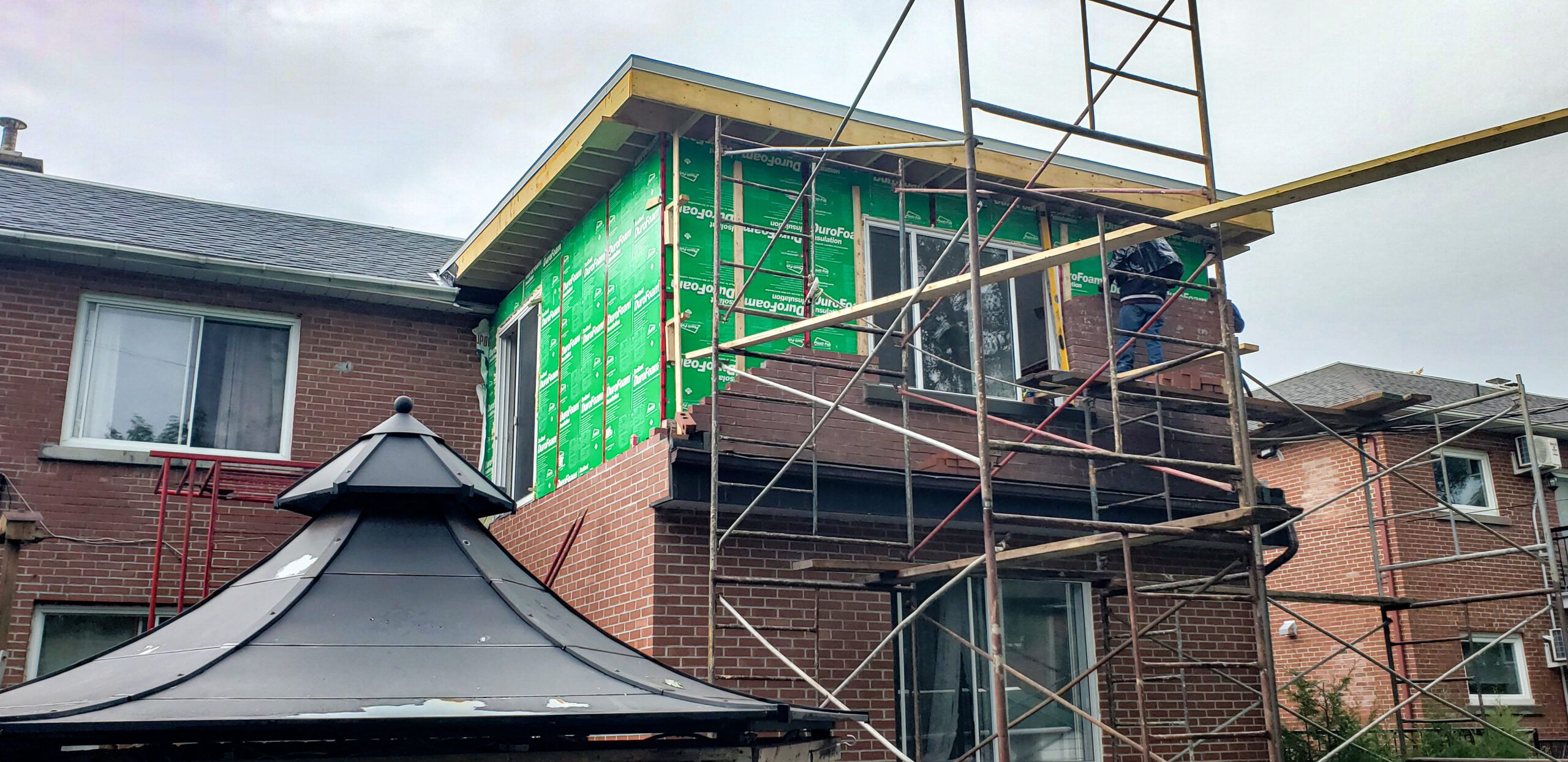 Green DuroFoam insulation panels being installed on a house exterior during renovation, showing energy-efficient home extension construction in Montreal.