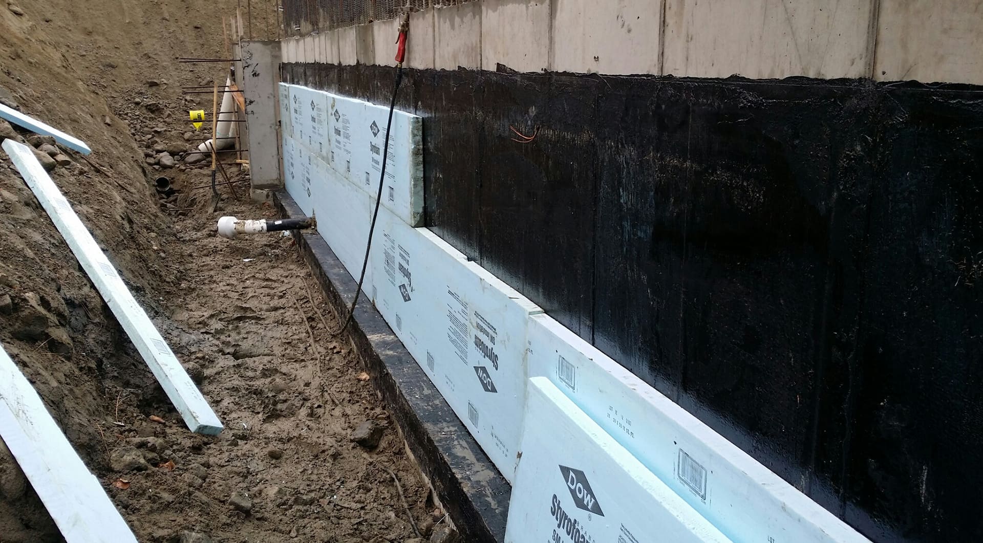 Basement waterproofing Quebec showing exterior foundation insulation with black waterproof coating and blue XPS foam boards to prevent moisture and improve energy efficiency.