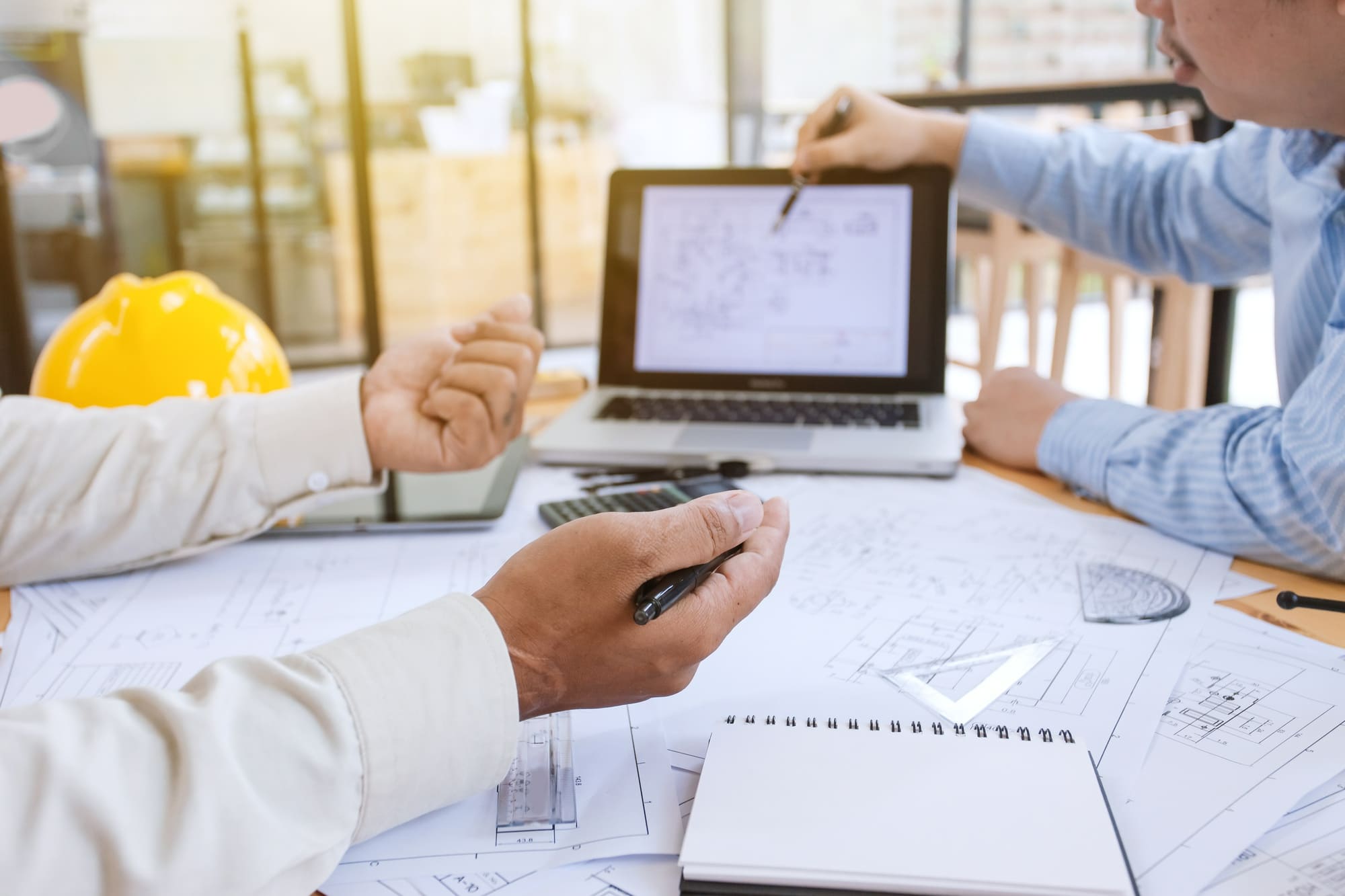 engineering services Quebec showing engineers and architects discussing construction plans with laptop helmet and calculator during project meeting.