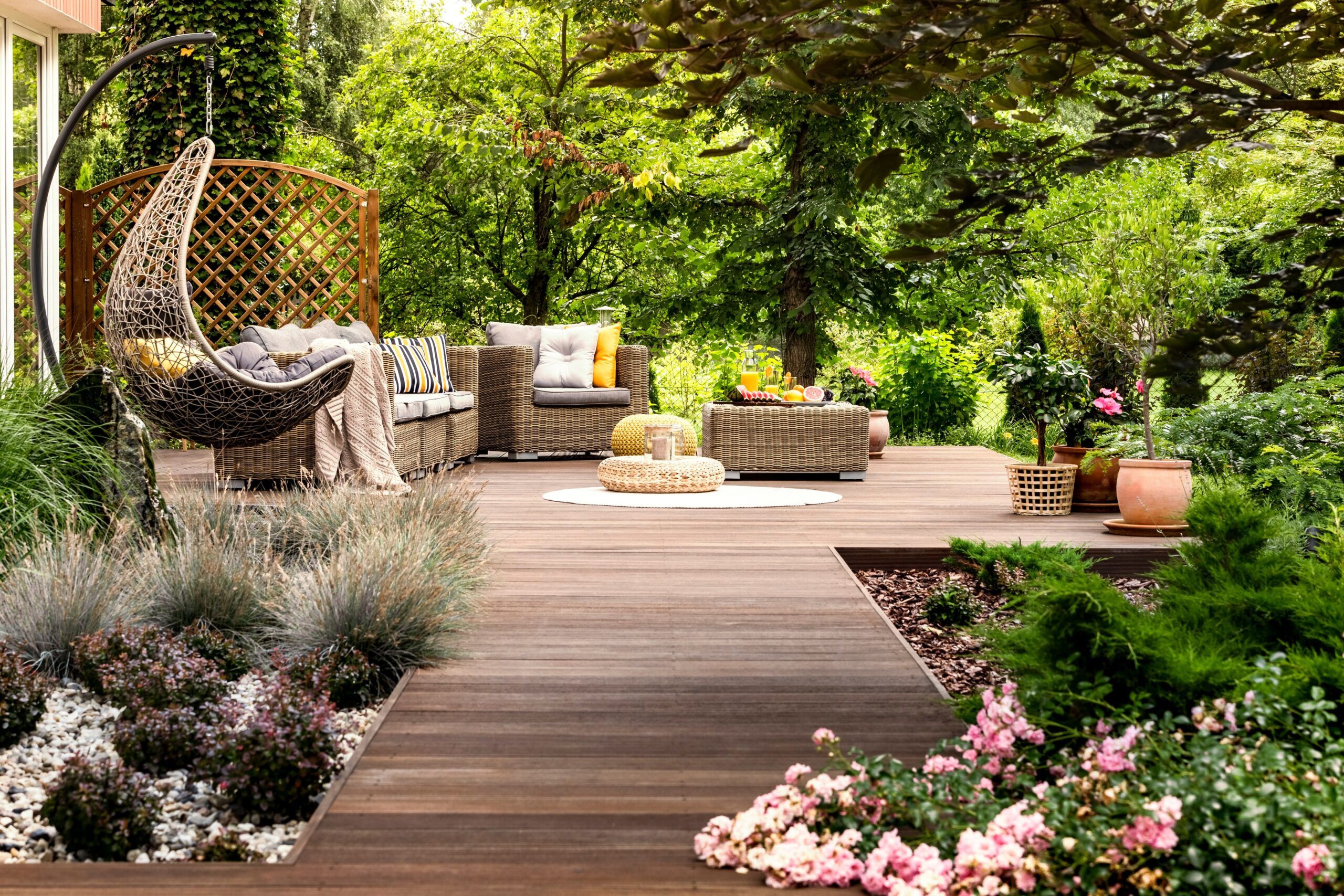 A beautifully designed garden and wooden terrace created by a professional Landscaping Services Quebec and Montreal, featuring outdoor furniture, a hanging chair, and lush green plants.