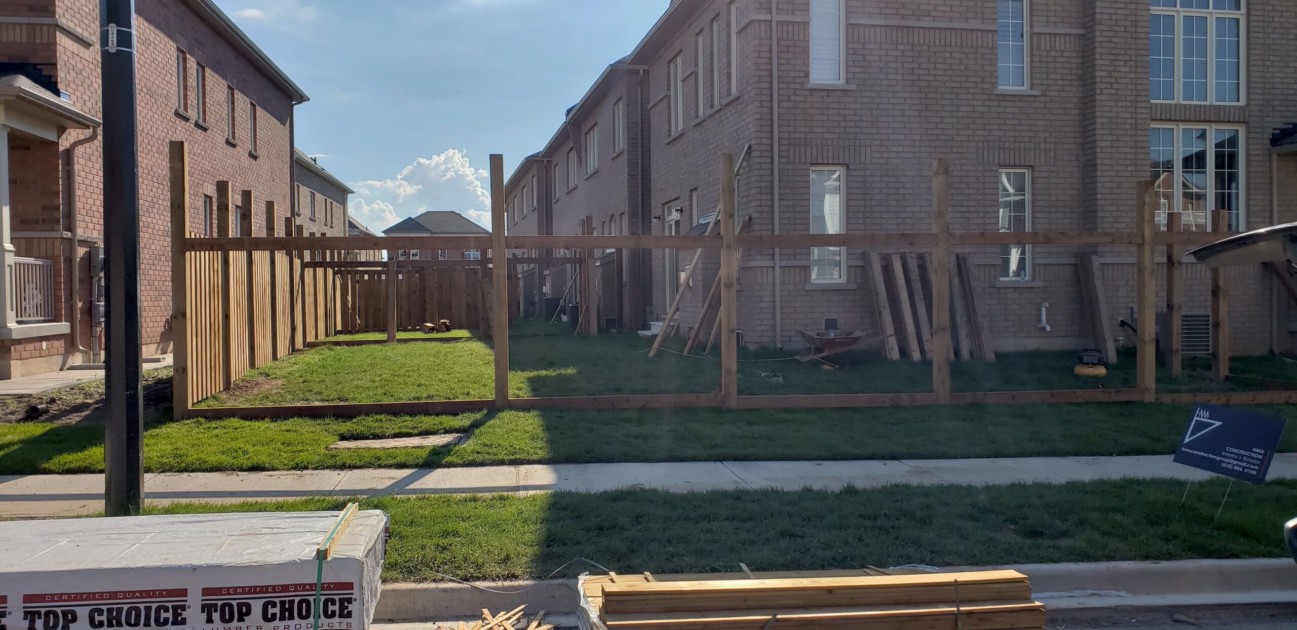 The Fence Buddy construction site showing workers building a wooden fence, with a company sign visible — illustrating fence installation services in Quebec that promote DIY efficiency using a 12-in-1 tool for various fence styles.