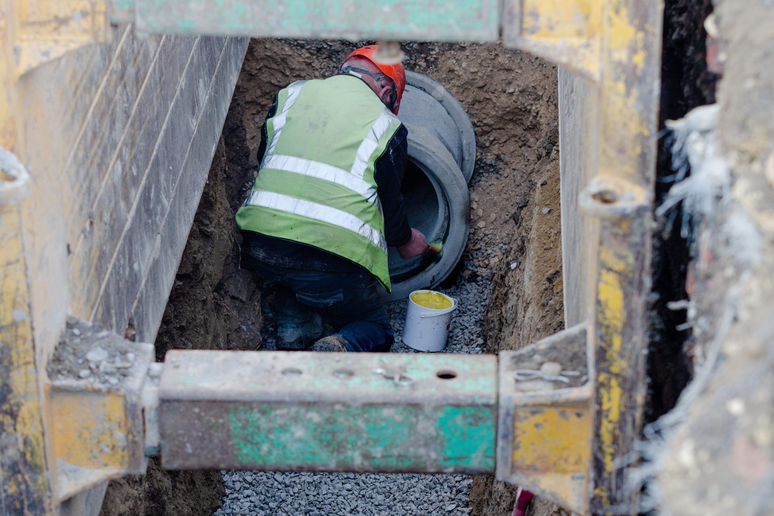 Electrical & Plumbing entrances Services Quebec showing the placement of a drainage pipe system with perforated tubing laid in a trench to direct excess water away from a building foundation.