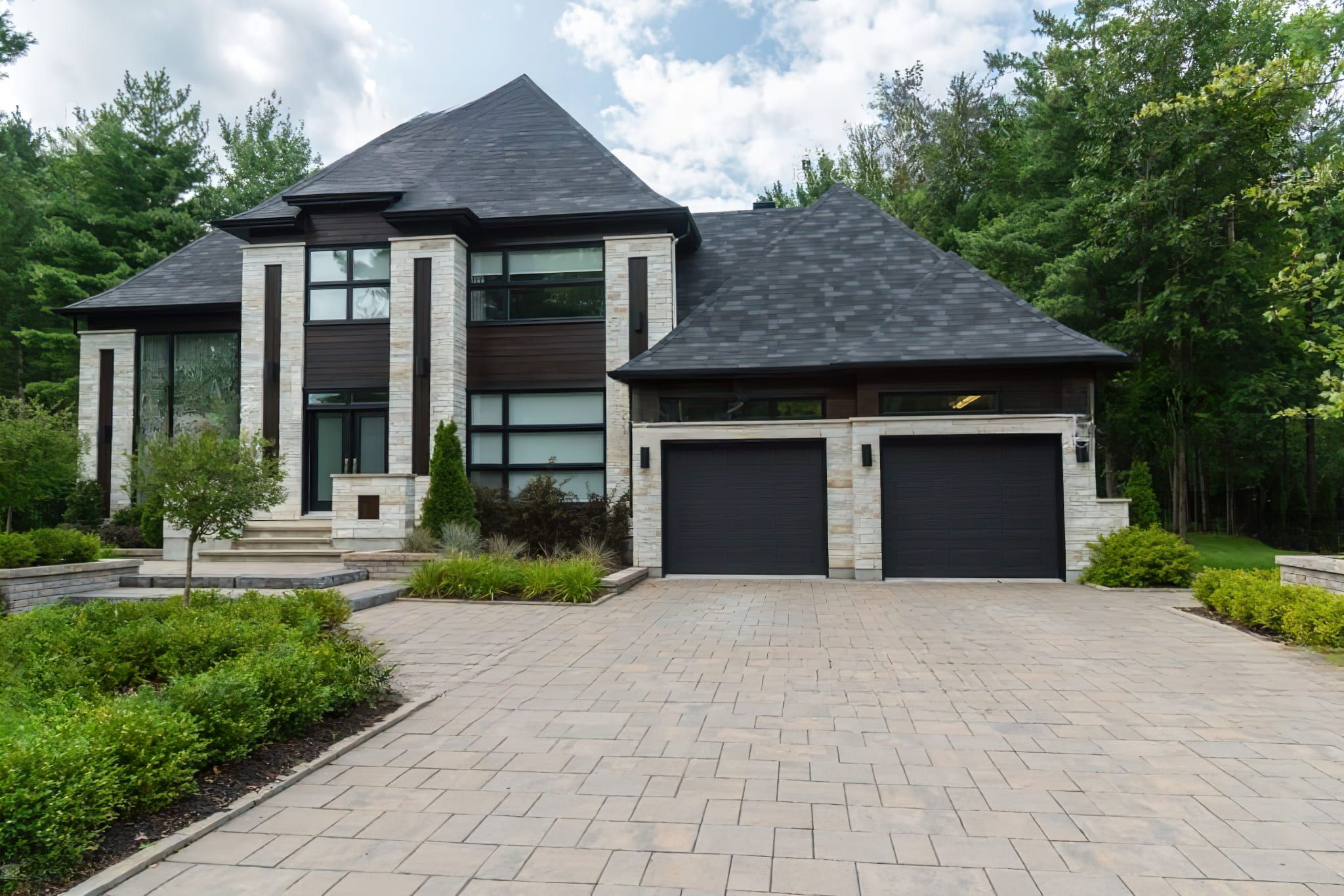 Modern two-story house with stone cladding, dark wood panels, and double garage doors, representing high-quality residential design supported by Interior Systems Quebec for energy efficiency and aesthetic excellence.