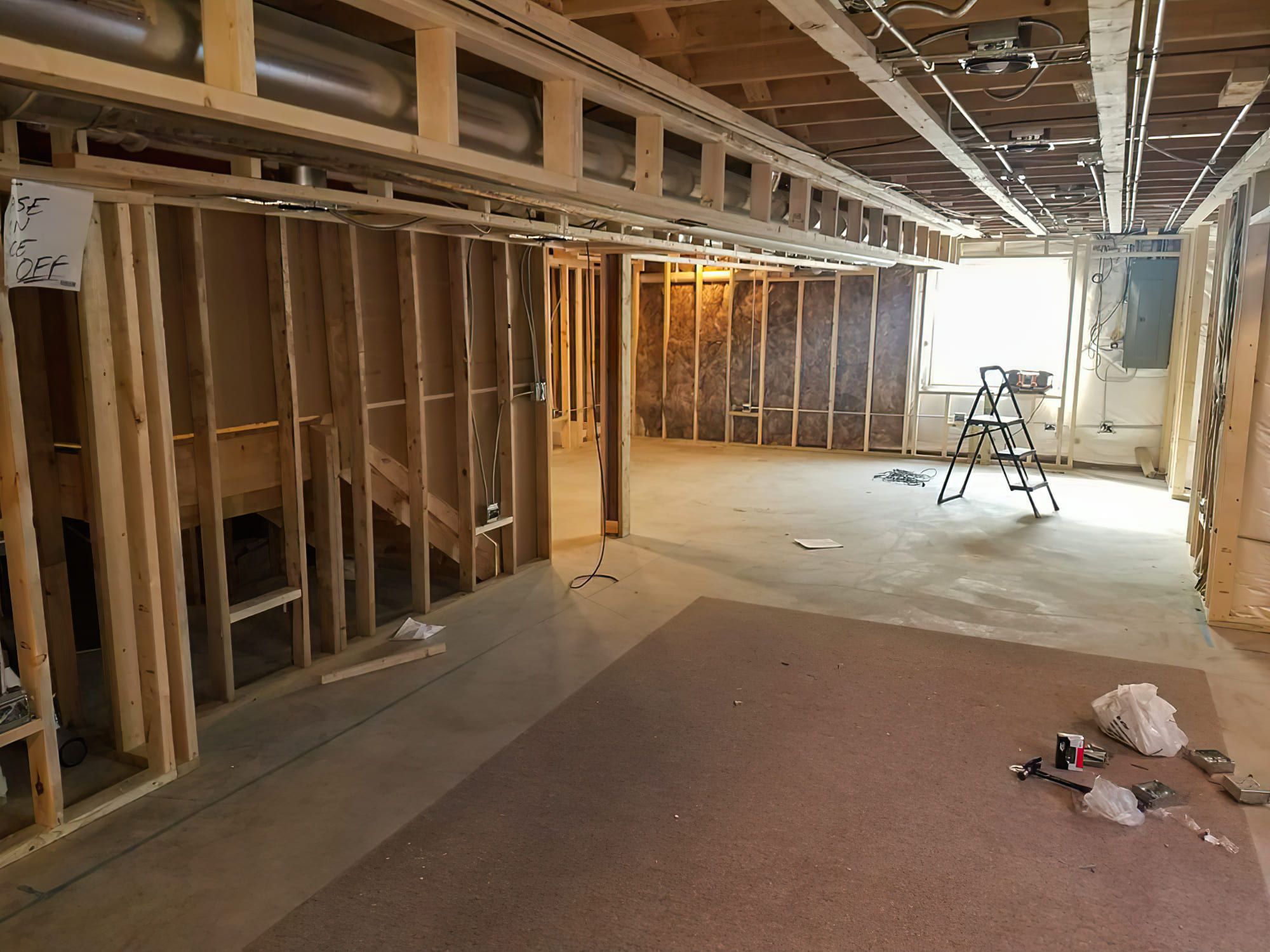 A basement under construction in Quebec and Montreal showing wooden framing with insulation between studs and an open ceiling exposing pipes and wiring — illustrating basement finishing and framing work in progress.