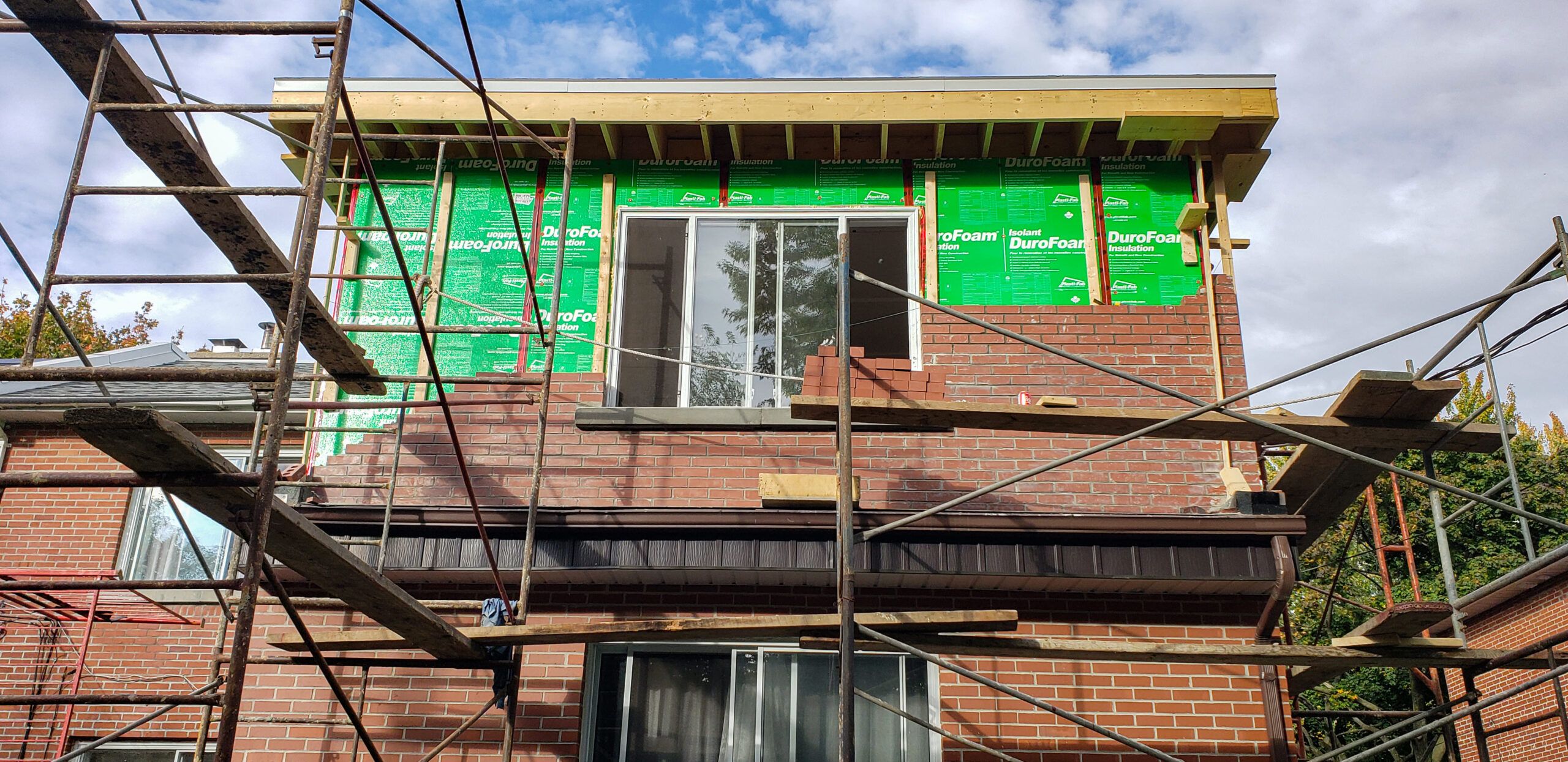 Brick house under construction with green DuroFoam insulation panels installed on the exterior walls, showing thermal insulation material used for home additions in Quebec.