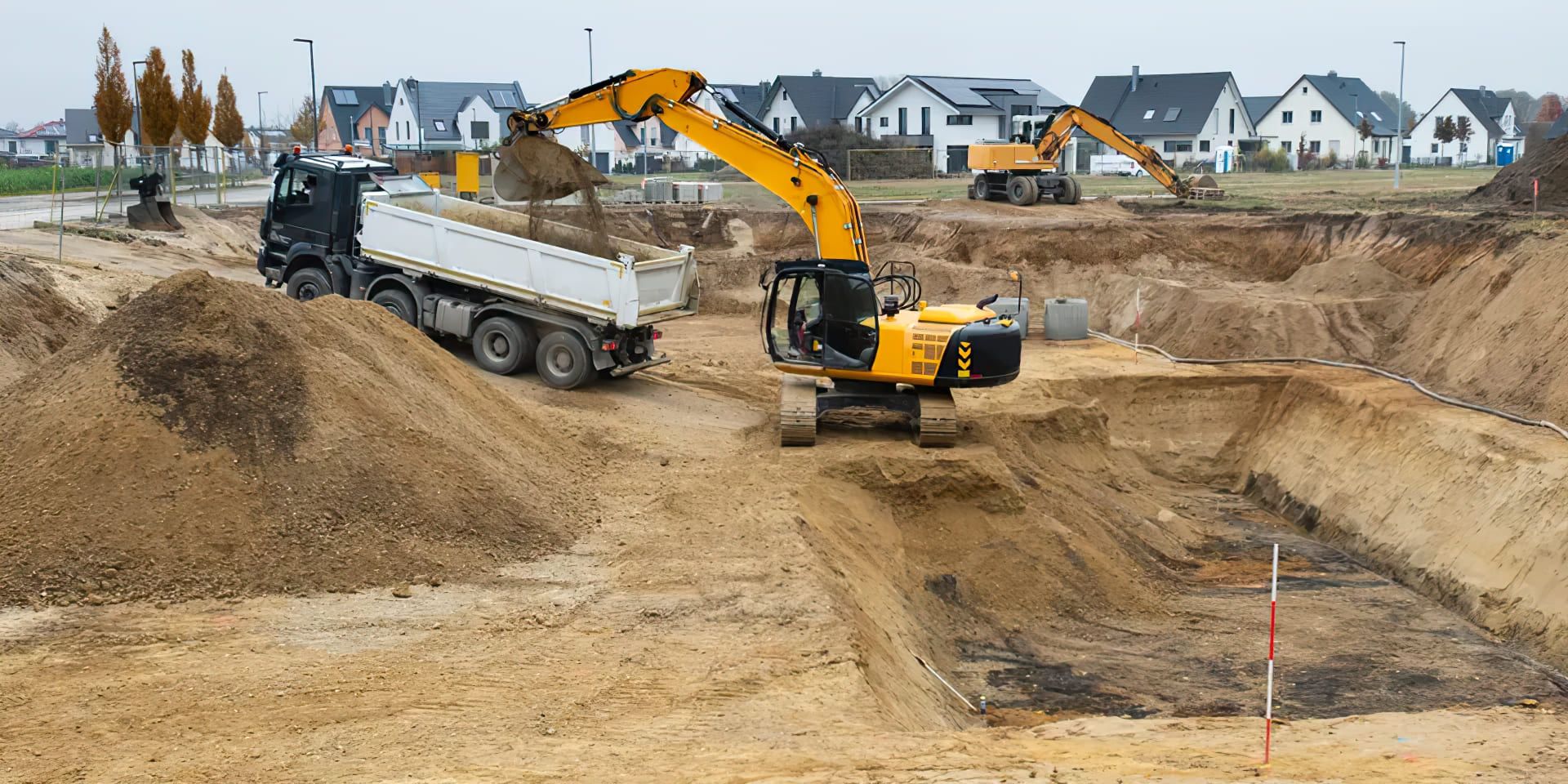 Residential excavation in Quebec showing an excavator loading soil into a dump truck on a construction site, highlighting earthmoving work essential for preparing building foundations.