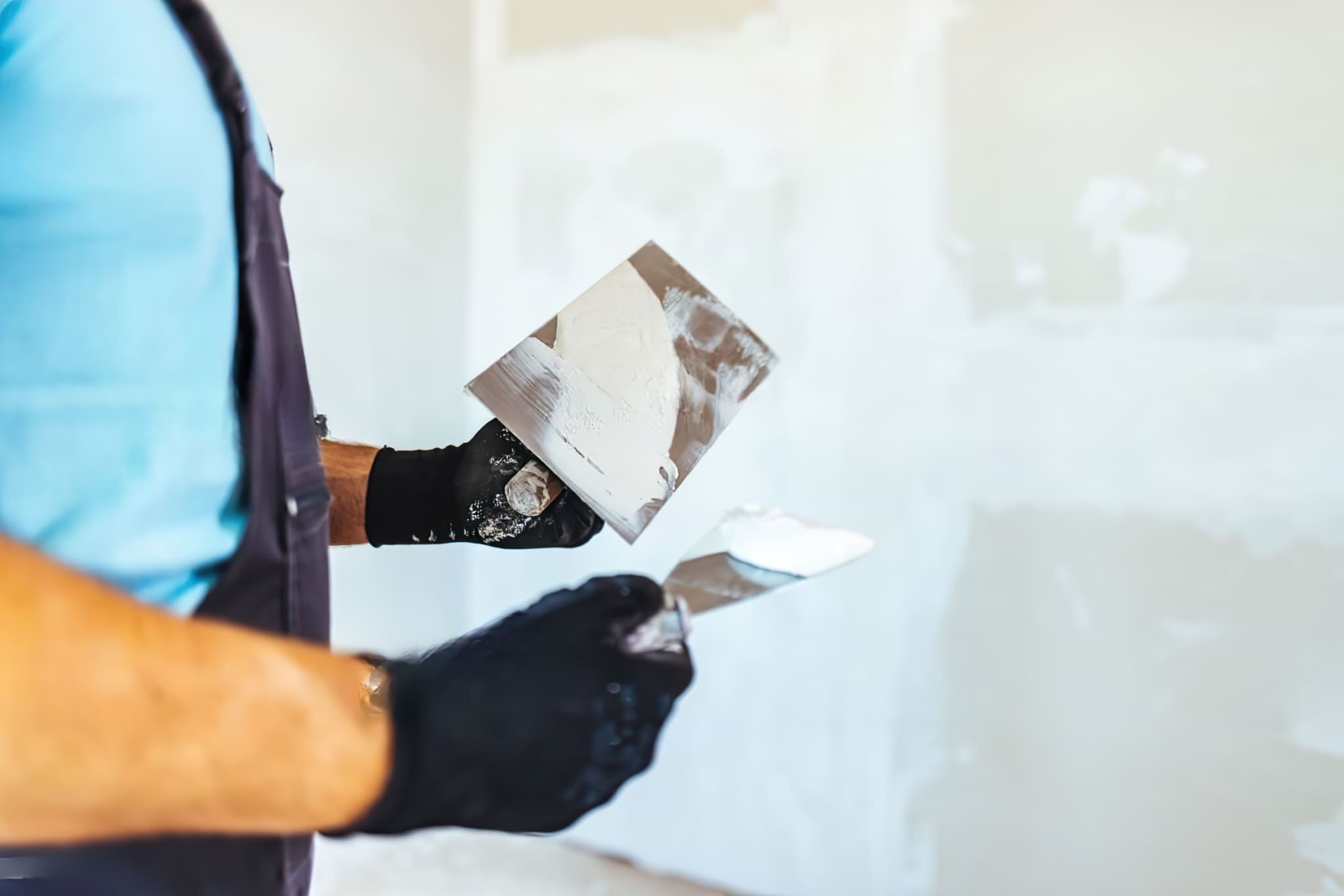 Home maintenance services Quebec showing a worker plastering or smoothing a wall as part of drywall finishing, applying joint compound to create a smooth surface; the process is part of interior construction using gypsum boards instead of traditional masonry.