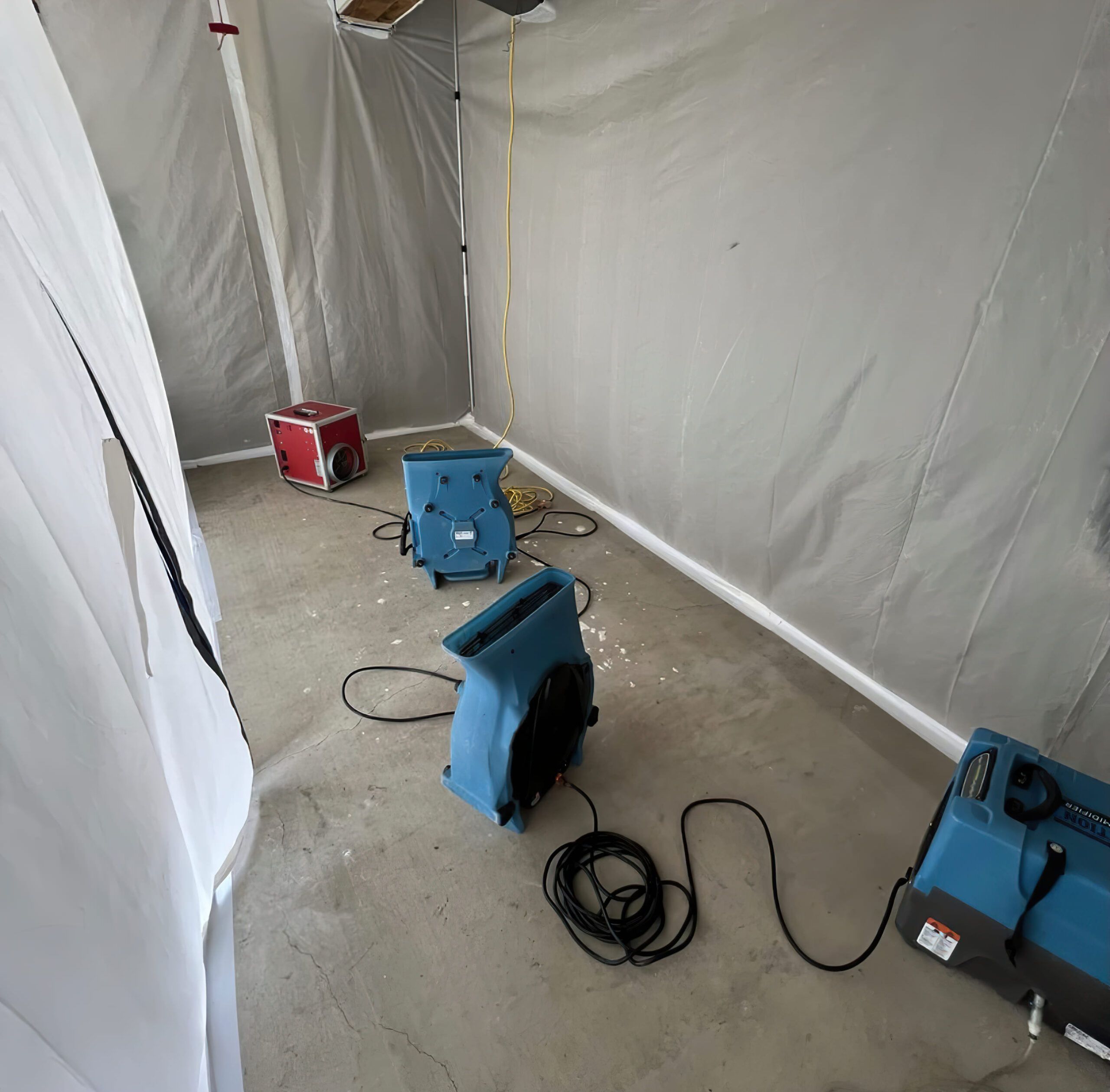 temporary drying setup after water damage in Quebec with industrial dehumidifiers, air movers, and plastic containment walls isolating the affected area to speed up moisture removal and prevent mold or structural damage.