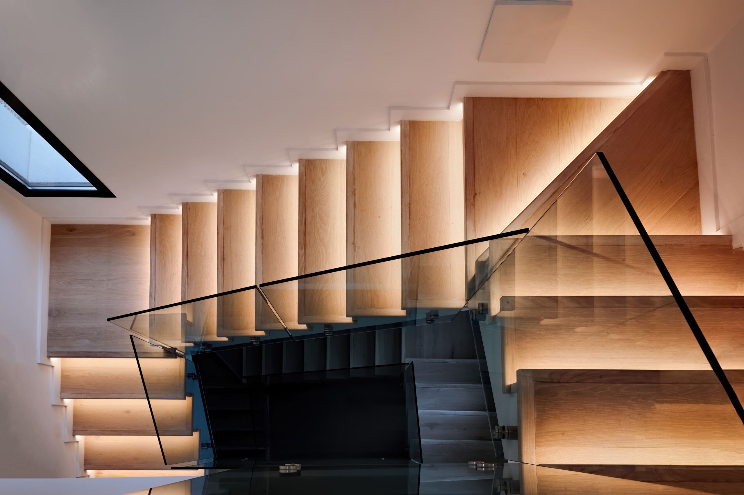 Interior stairs installation in Quebec featuring a modern wooden staircase with side LED lighting, glass and metal railings, and a floating design that combines natural materials with minimalist, contemporary aesthetics.