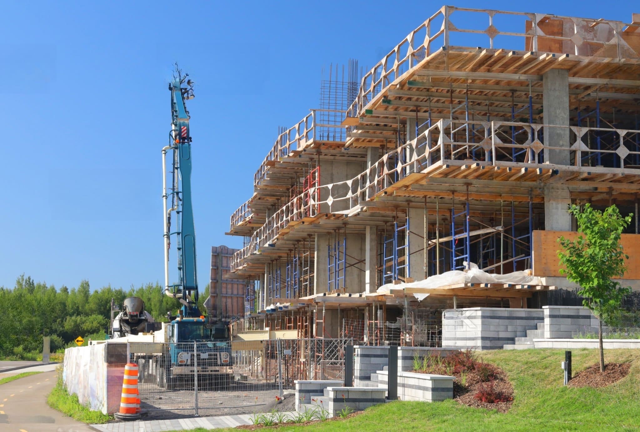 construction site in Quebec with multi-story building under construction, concrete pump in operation, scaffolding, rebar, and early landscaping work indicating new building development.