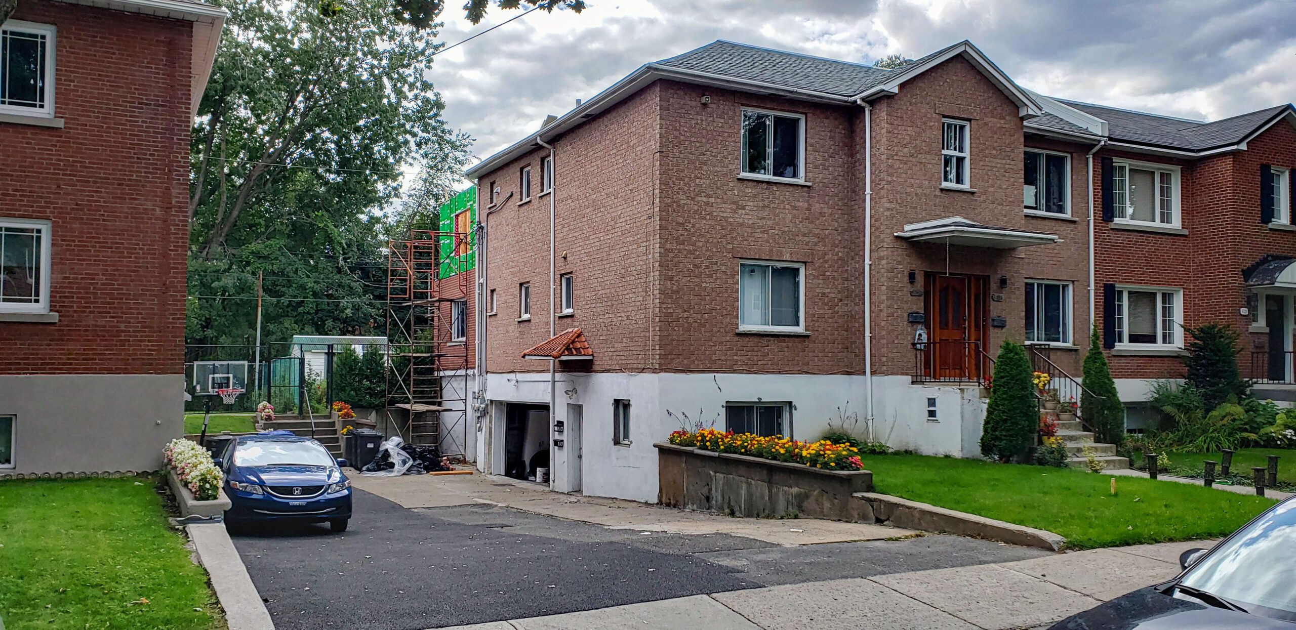 Red brick multi-family house at 19 Strathcona Avenue in Ottawa, Ontario, with multiple entrances, parked cars in the driveway, and a basketball hoop in the background.