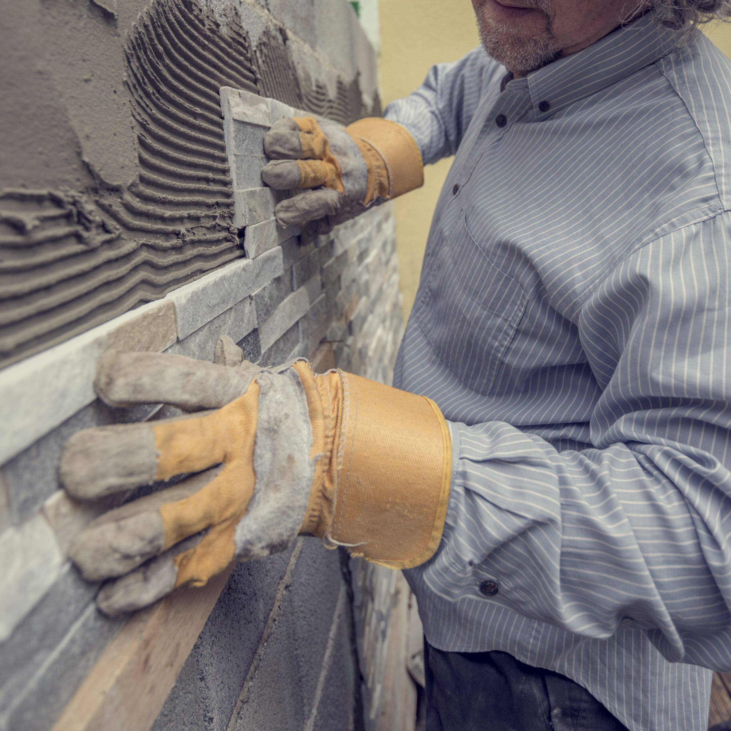 A worker installing wall cladding tiles as part of Exterior Finishings Services in Quebec, showing veneer panels used to protect building walls and enhance their appearance.