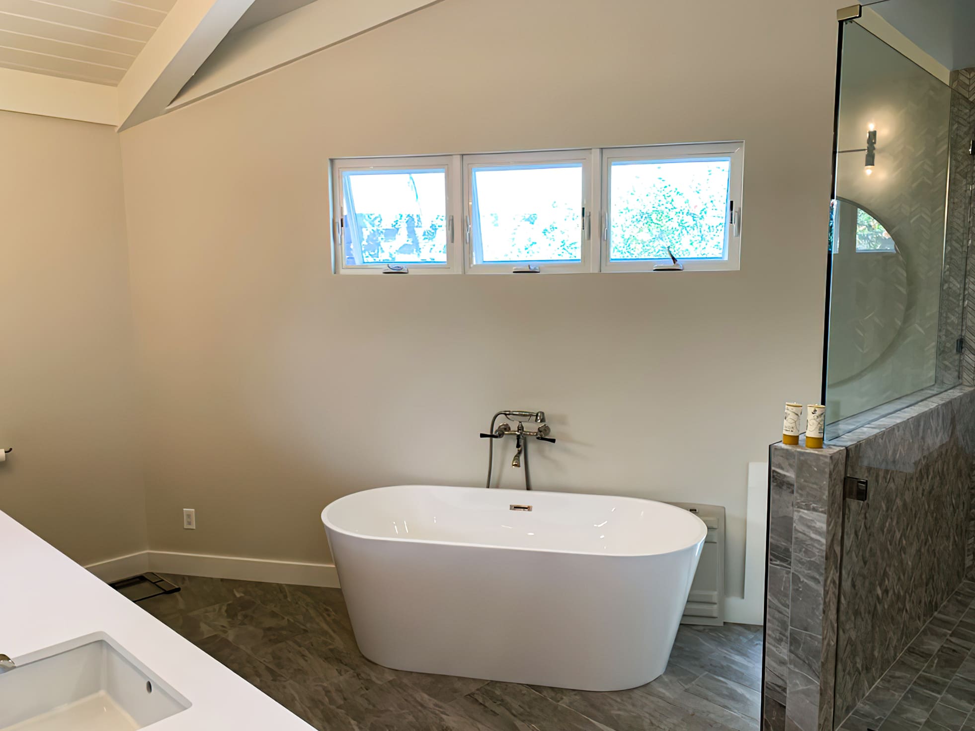 Modern bathroom with freestanding oval tub, glass shower, wood-look tile flooring, and natural light, representing contemporary bathroom design and remodeling in Quebec focused on comfort and relaxation.