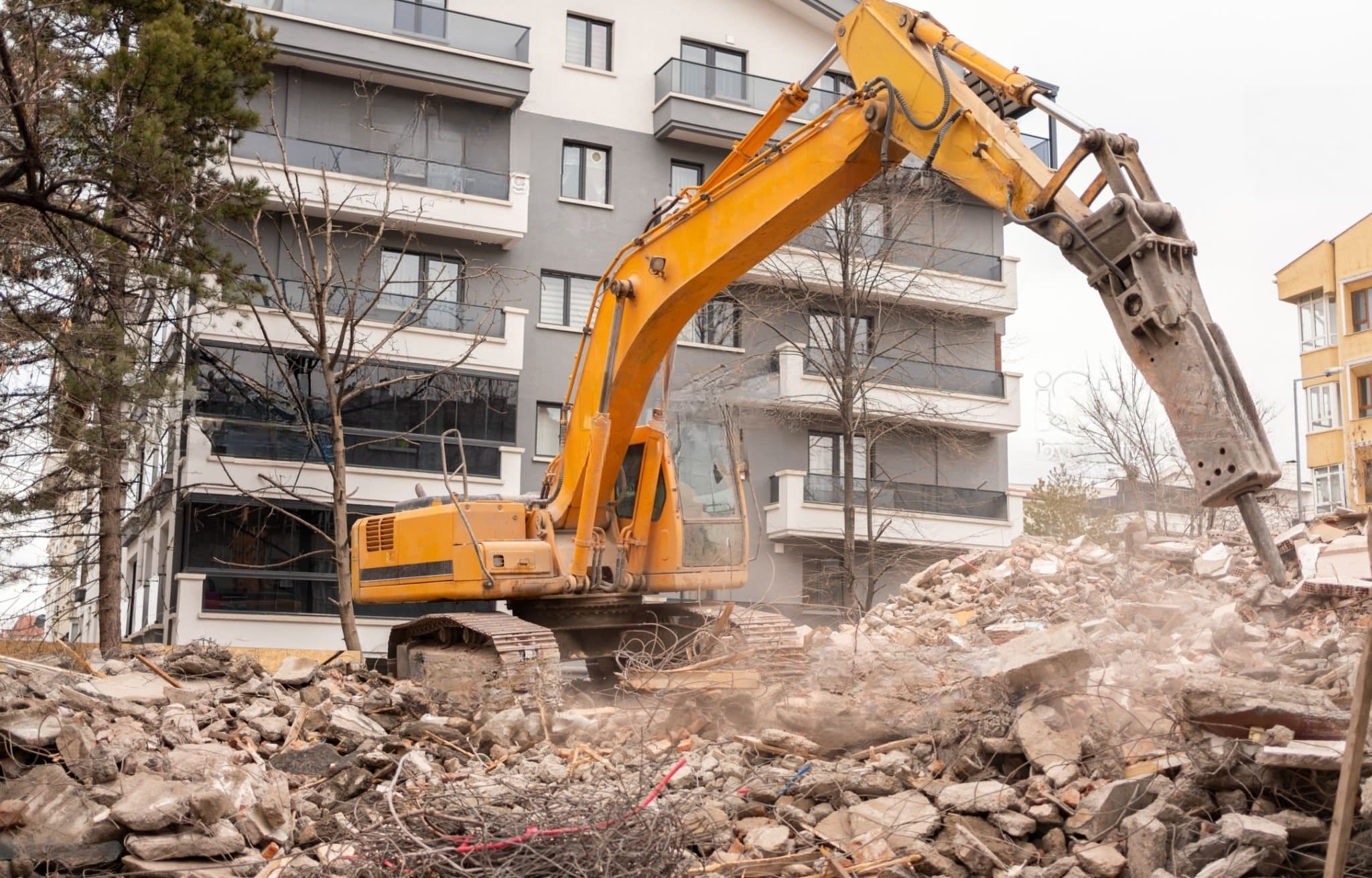 Commercial Demolition Montreal showing an excavator with a hydraulic hammer in action during the controlled demolition of a commercial building site.