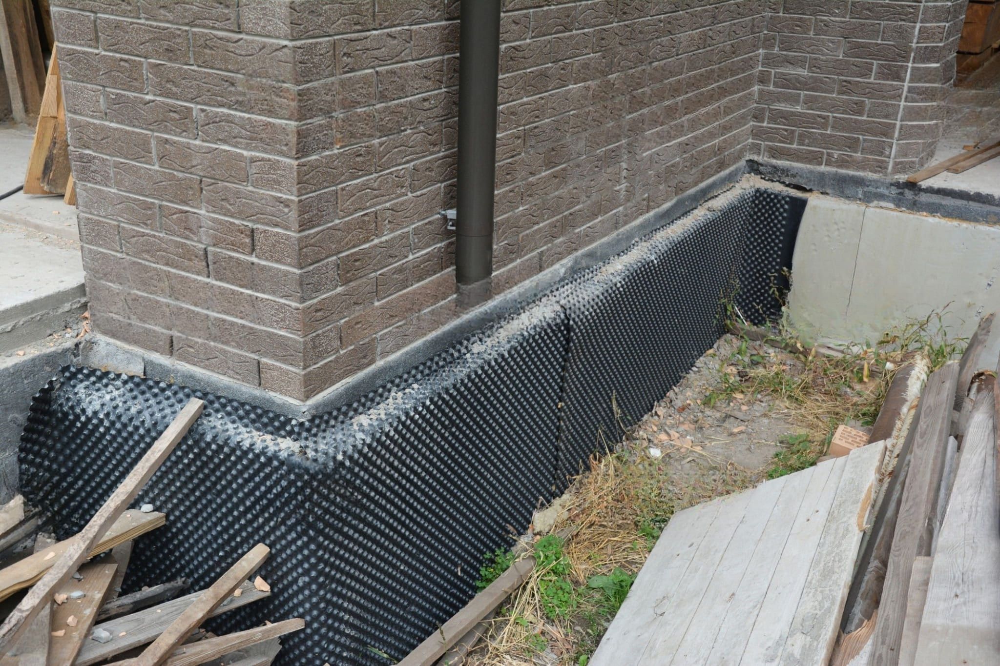 Waterproofing & French Drain Services Quebec showing exterior basement wall waterproofing with a black dimpled membrane that protects the foundation and directs water away from the structure.