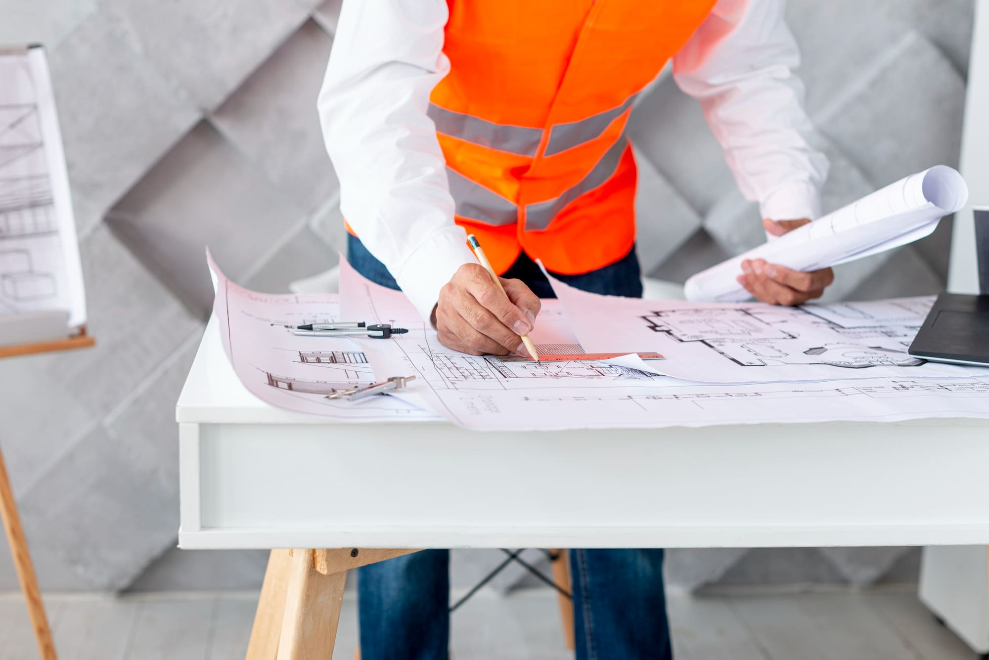 architectural design Quebec showing architect or engineer in safety vest reviewing and marking building blueprints on table during project planning.