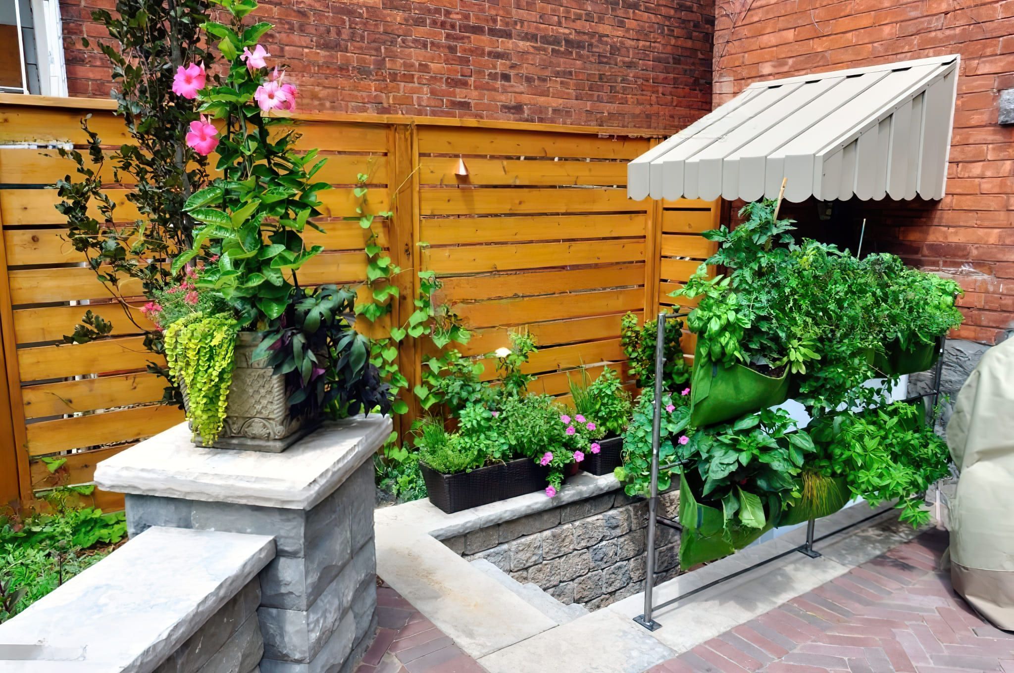 Walkout basement construction in Quebec depicted through a landscaped backyard with a stone staircase leading to a lower-level entrance, surrounded by wooden and brick walls, lush plants, and a vertical garden under a retractable awning.