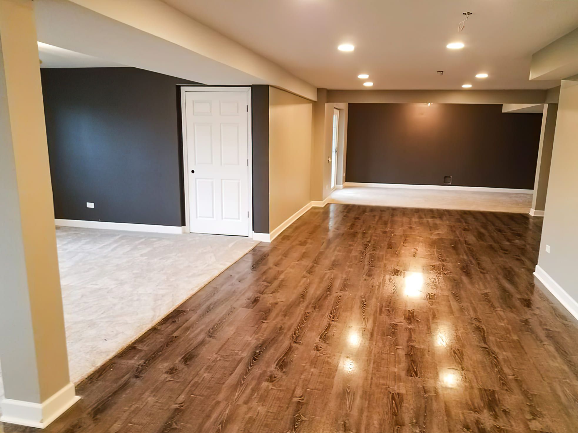 Basement Finishing Services Quebec featuring a mix of carpet and hardwood flooring, two-tone painted walls, and recessed ceiling lights — showcasing a modern basement upgrade with moisture-resistant engineered wood.