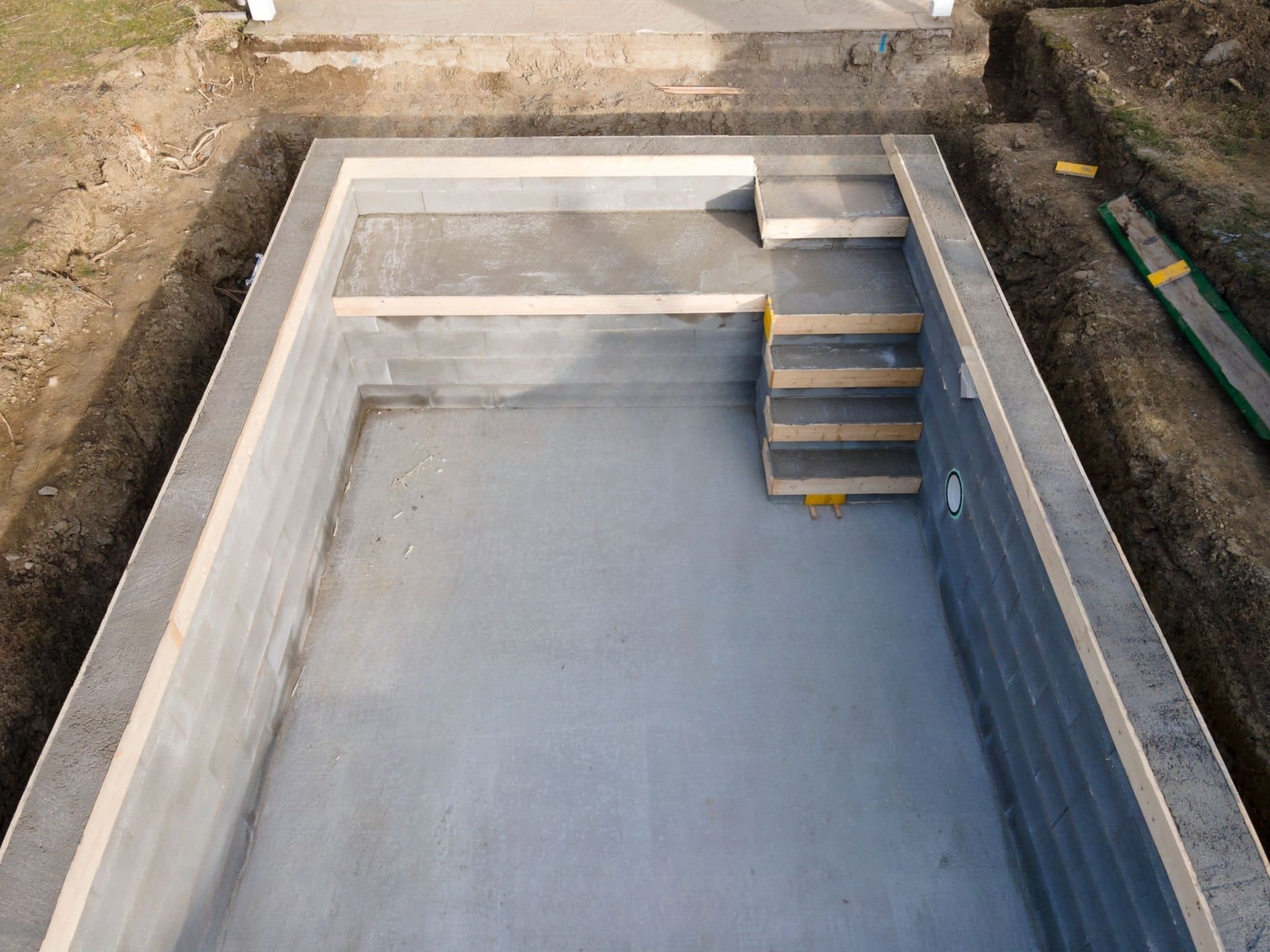 custom pool builders Quebec — construction of a concrete swimming pool with integrated stairs, reinforced walls made of concrete blocks, and formwork in an excavated area for a durable custom-built design.