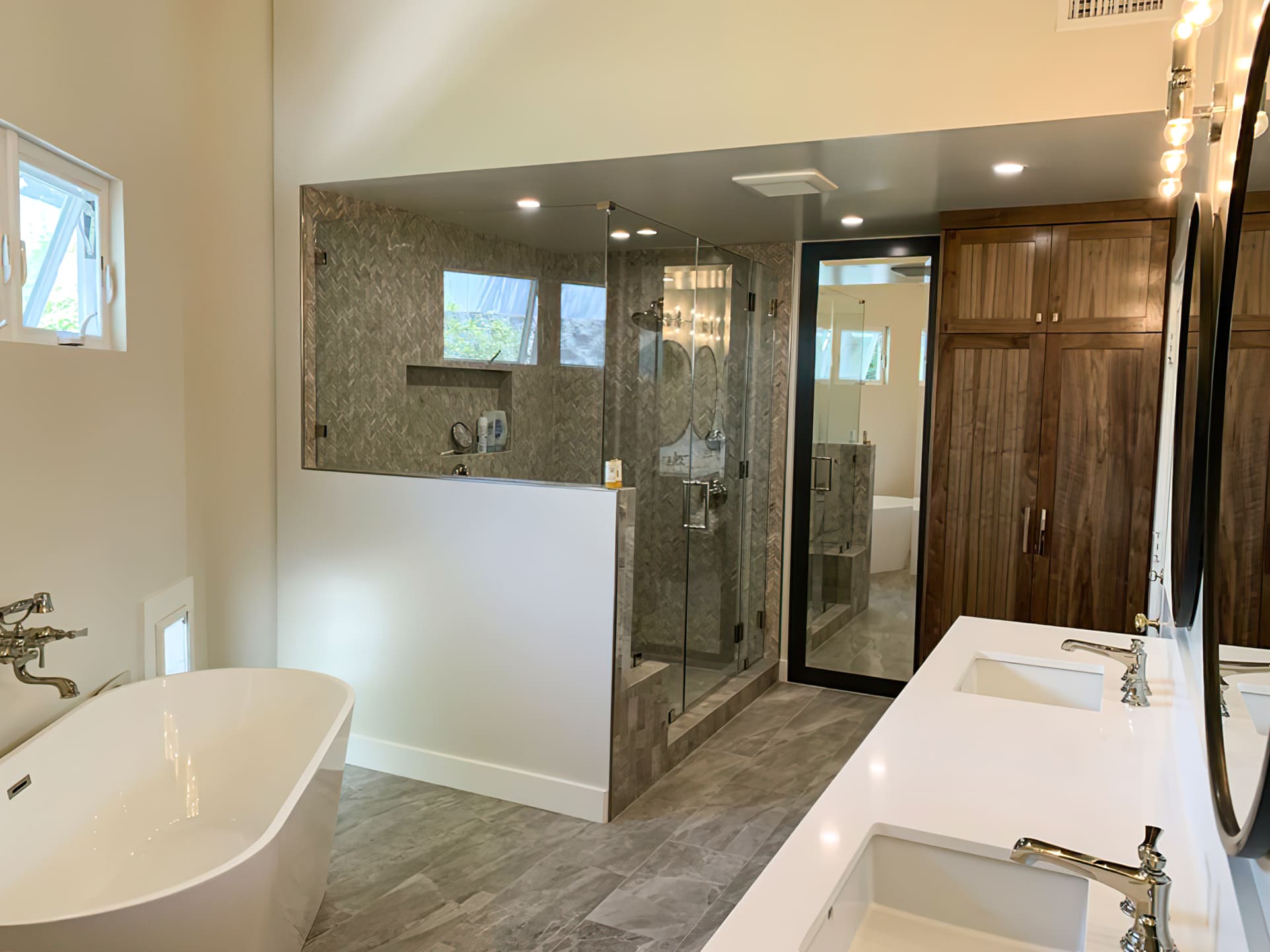 Modern renovated bathroom with freestanding tub, walk-in glass shower, double vanity with white countertops, and dark wood cabinets, showcasing luxurious bathroom design and remodeling in Quebec.