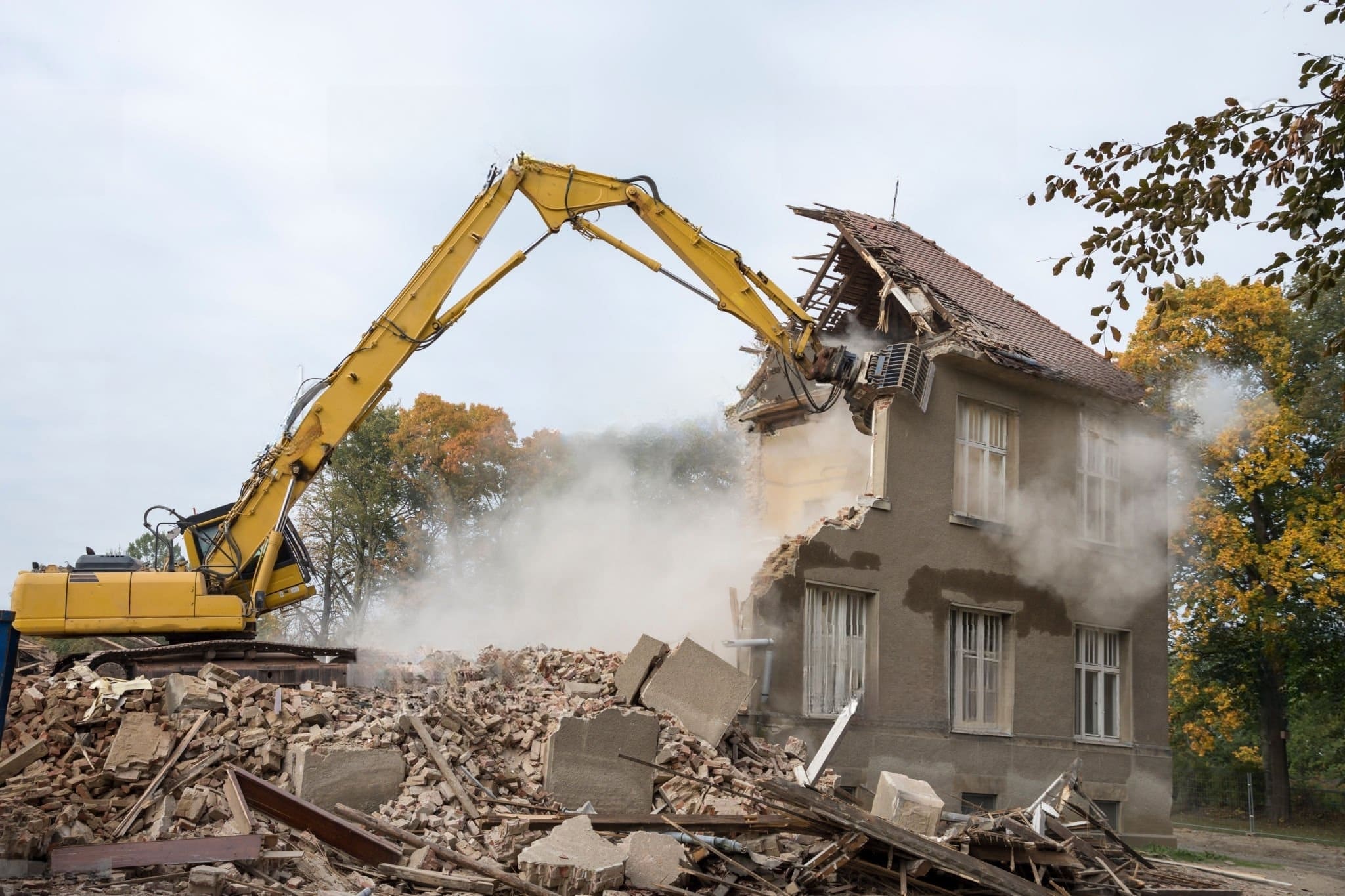 Building Demolition Montreal with an excavator tearing down an old house, illustrating the controlled removal of unsafe structures to clear space for new construction projects.