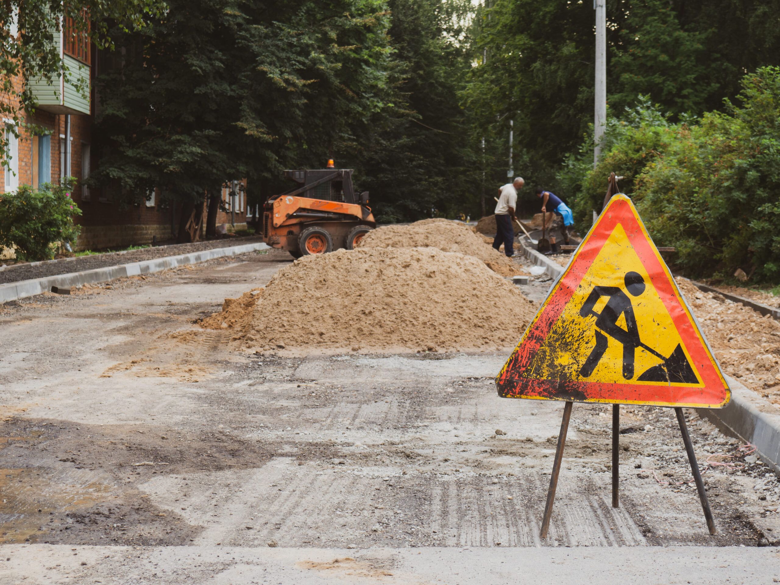 Electrical and plumbing entrances services in Quebec showing an outdoor construction site with two workers, a small excavator, and a warning sign as they prepare underground utility connections for electrical and plumbing systems.