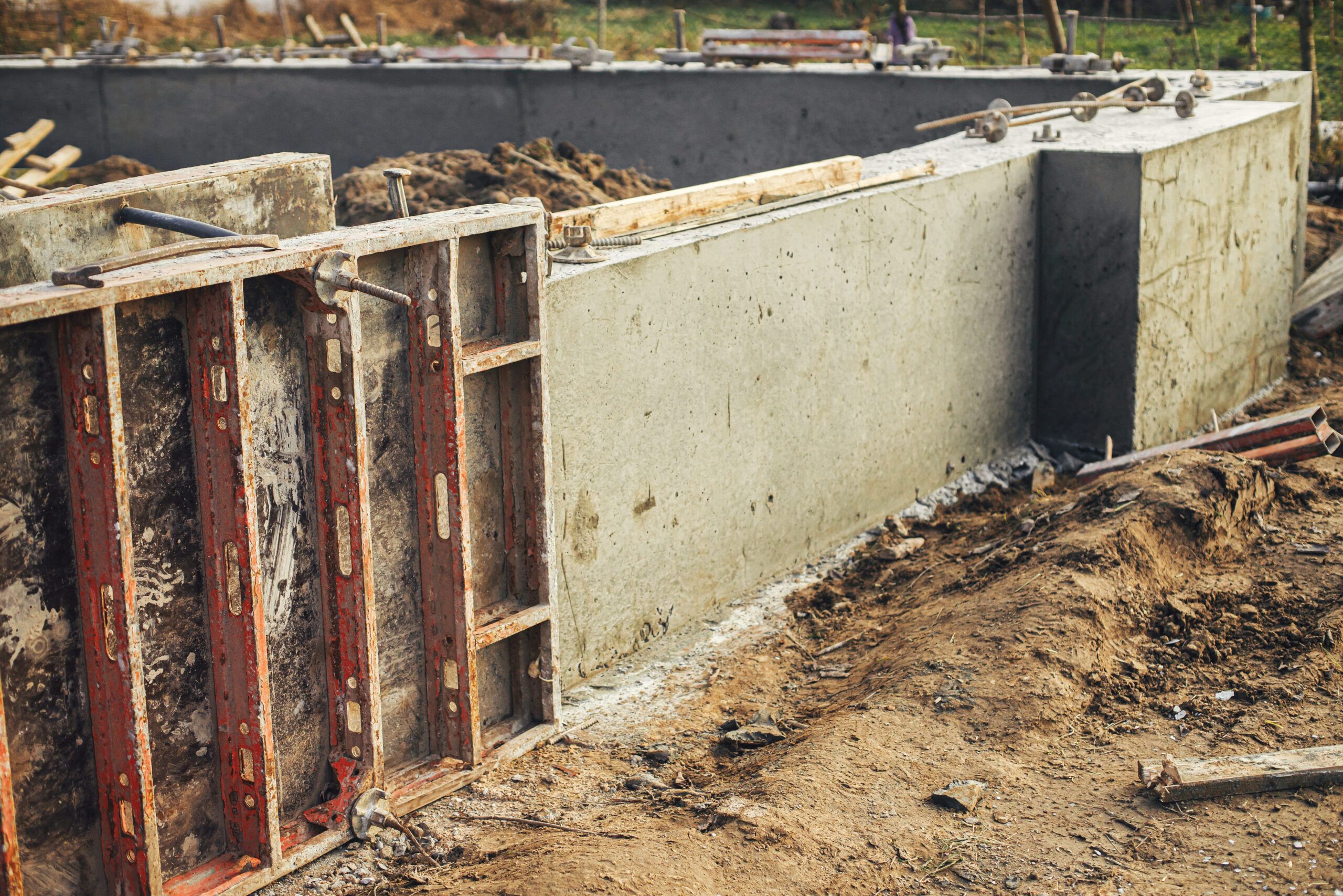Construction site in Quebec showing a concrete foundation with red metal formwork panels, excavated soil around the structure, and a gravel base layer used for frost protection beneath the poured concrete.