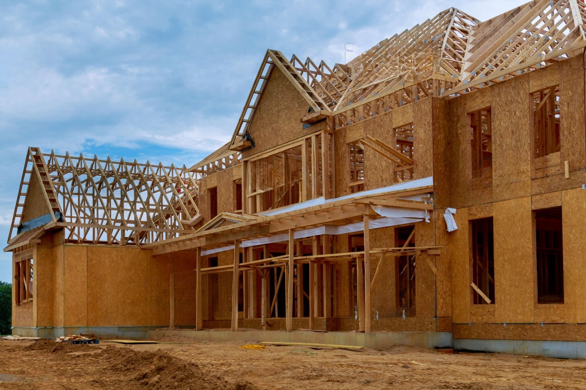 new construction Quebec showing a wooden house frame in the rough construction phase with visible roof trusses, OSB wall panels, and unfinished exterior structure.