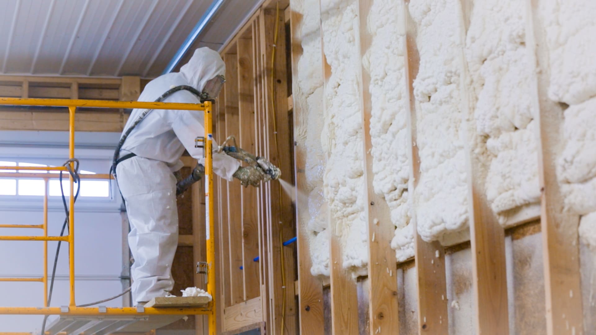 Insulation services Quebec showing a worker in protective gear spraying polyurethane foam insulation onto a wall to create a seamless, high-performance thermal and sound barrier.