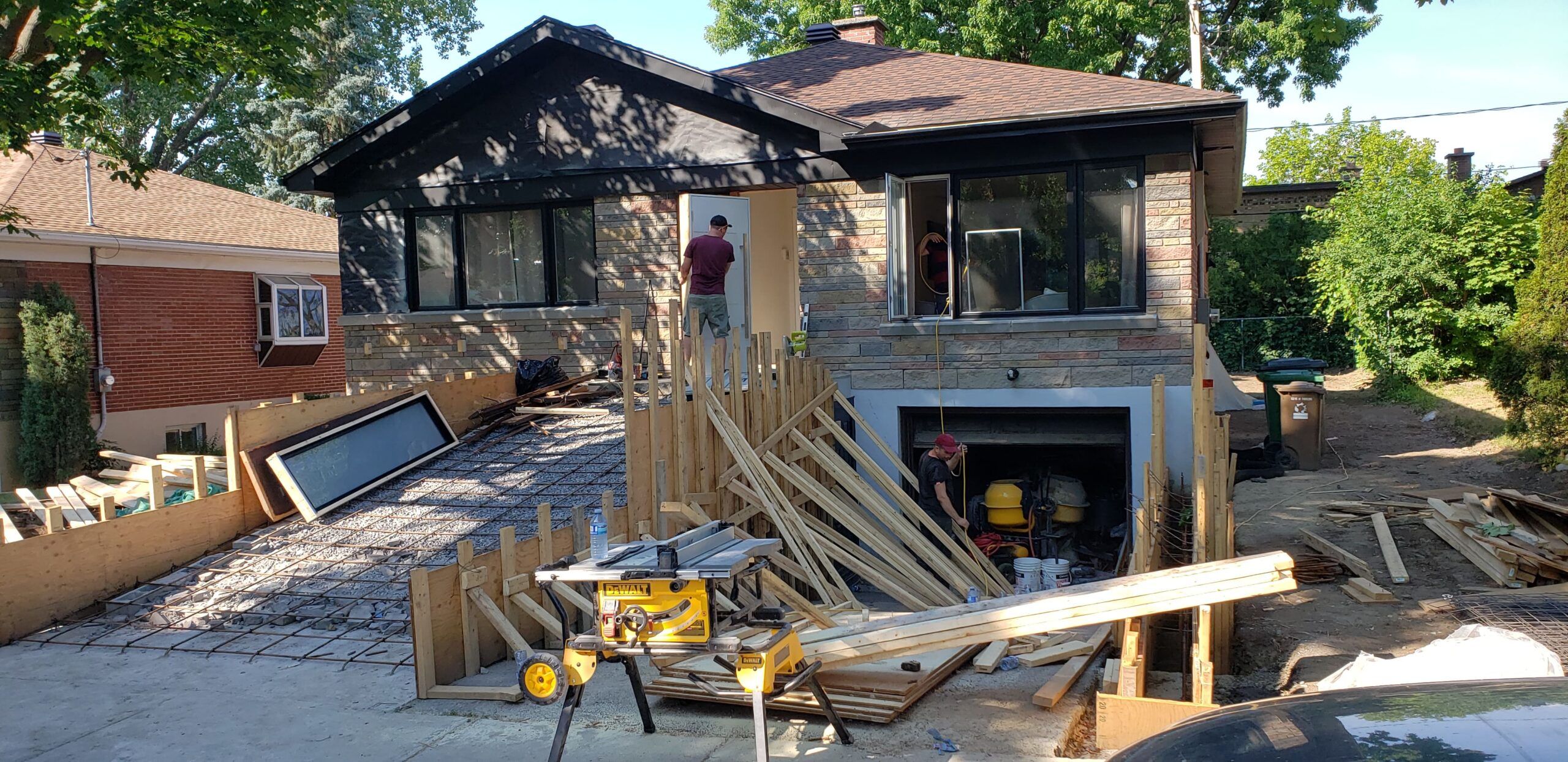 Home renovation and foundation repair project in Quebec showing workers reinforcing the house foundation with steel rebar and construction materials such as wood planks, scaffolding, and tools on site.
