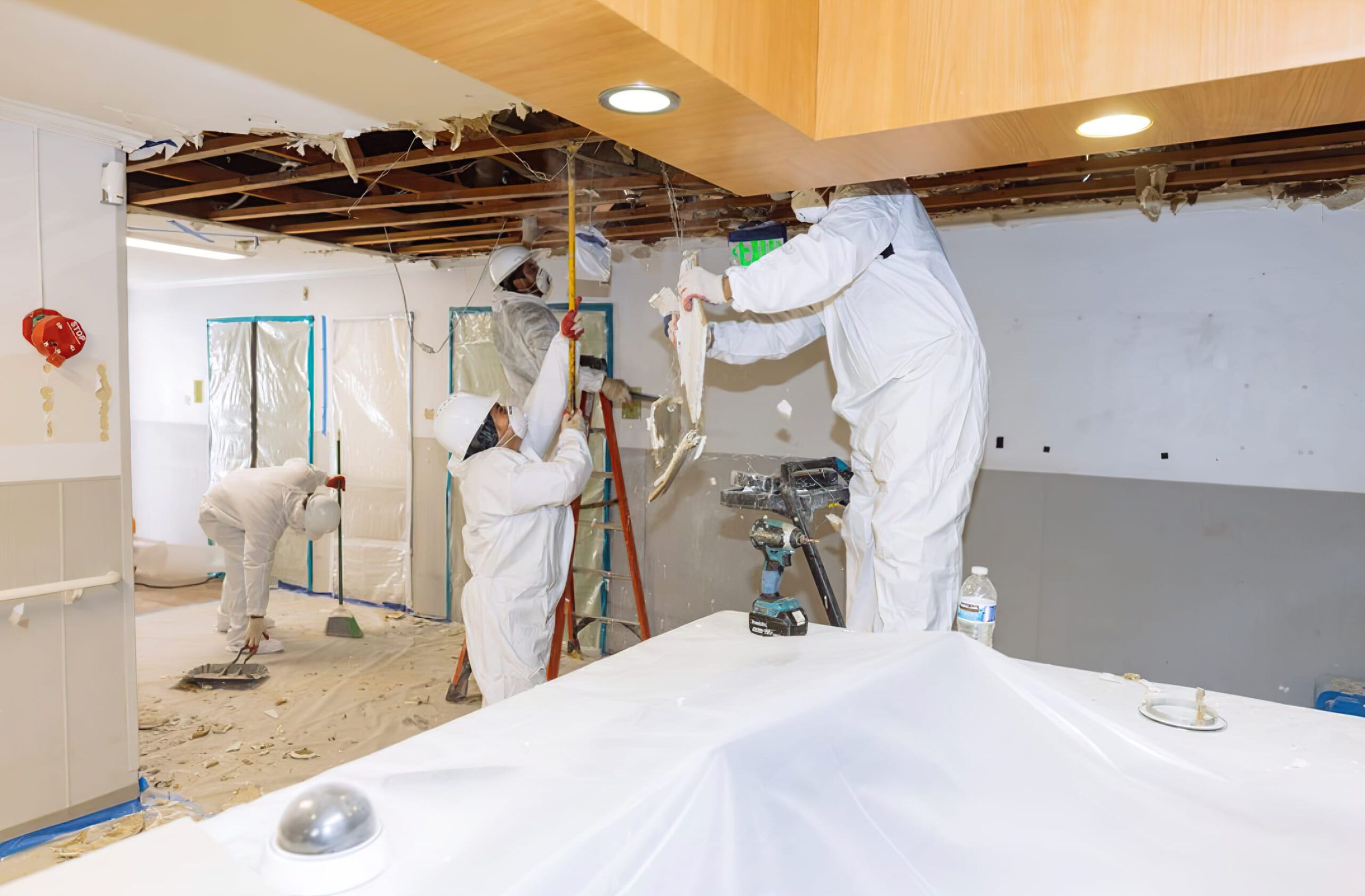 decontamination services Quebec team wearing protective suits masks and gloves removing ceiling materials during renovation or asbestos mold remediation with plastic sheeting for dust containment.