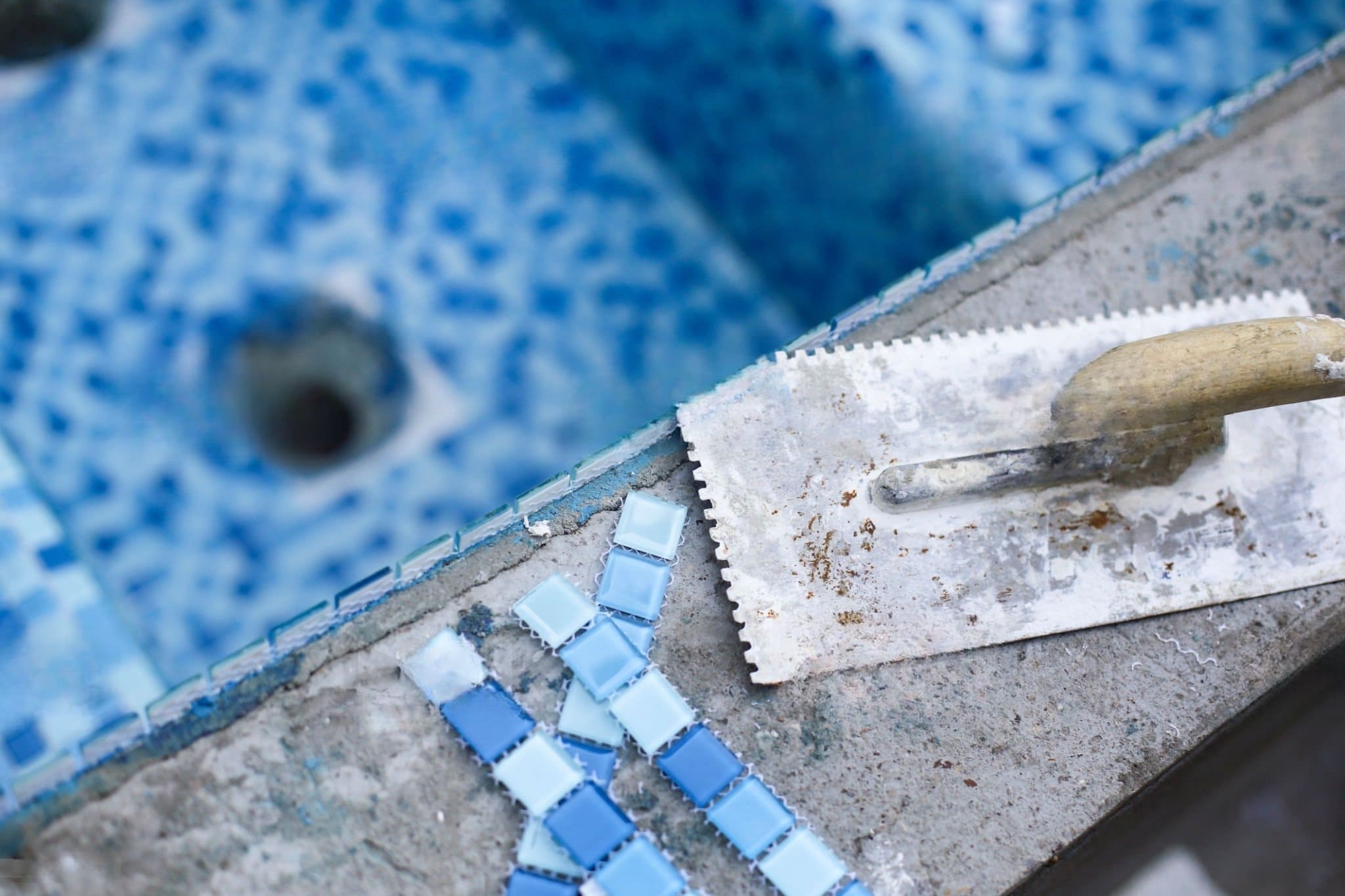 Swimming Pool Installation Quebec — tiling of a swimming pool using a trowel to apply adhesive; waterproof tiles are being installed to ensure a durable, leak-resistant pool surface.