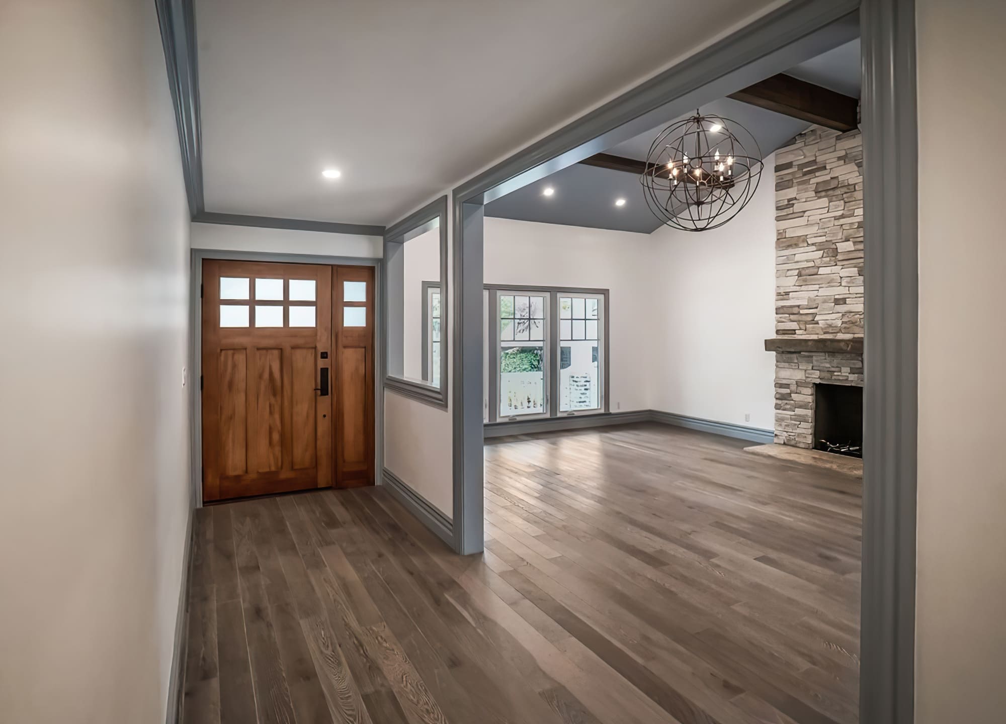 Property renovation Quebec featuring a mid-century modern entryway with clean lines, warm tones, natural materials like wood and stone, large windows, and a striking chandelier.