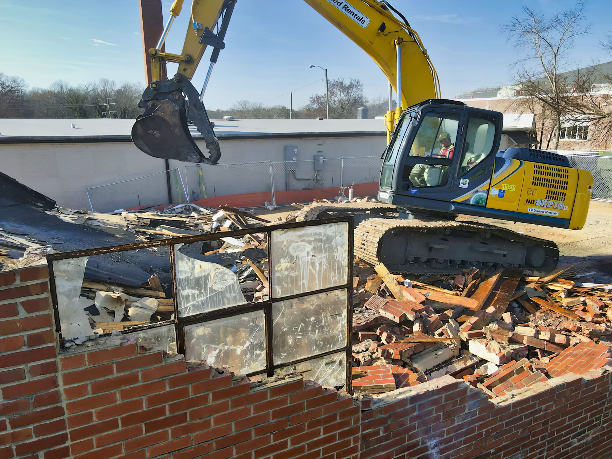 Demolition Services Montreal featuring a yellow SK210 excavator from United Rentals tearing down a building, showcasing typical equipment used for medium-scale demolition and construction projects.