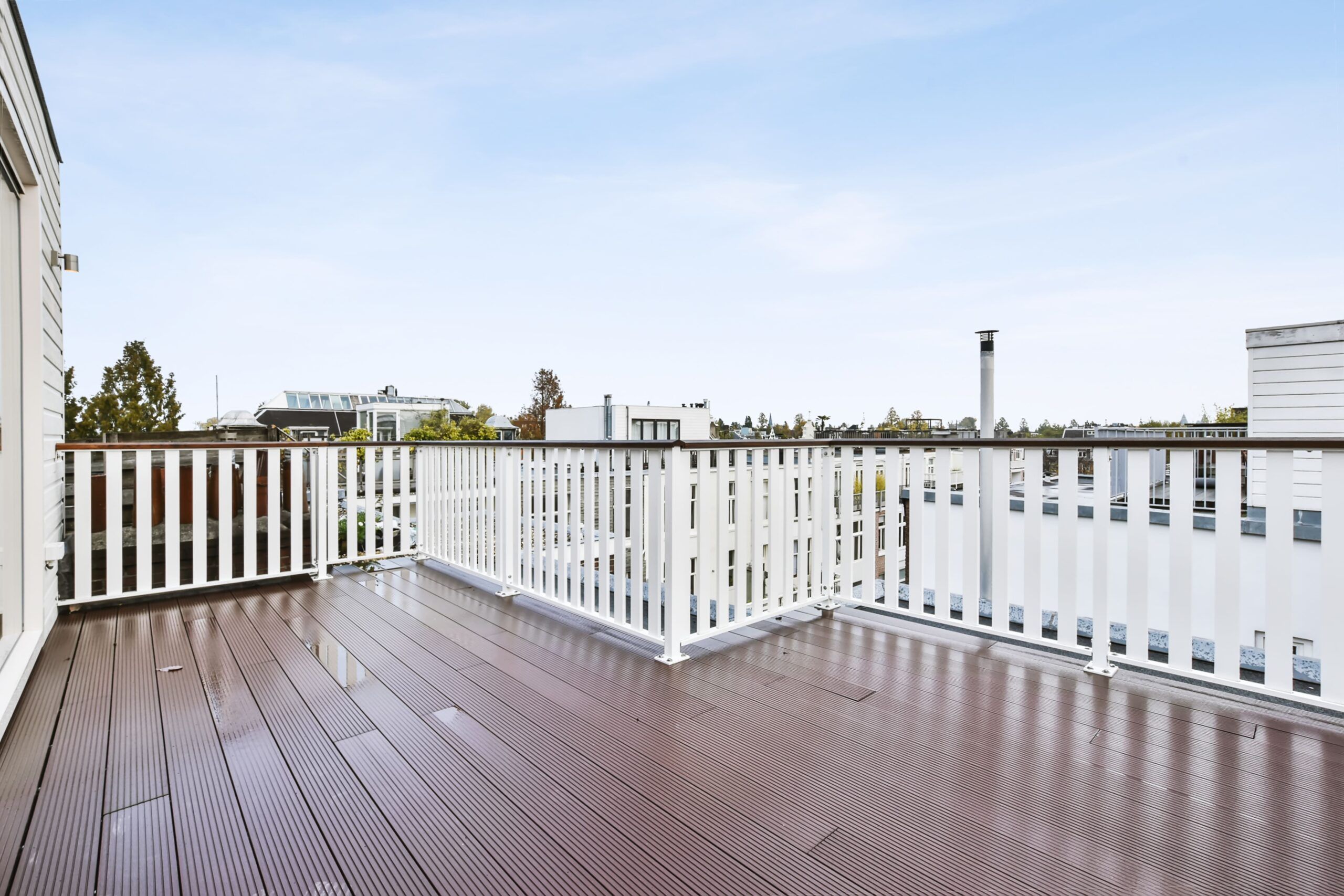A modern balcony with white vertical railings and dark wood-like decking made from WPC material, showing clean architectural lines and quality design typical of Fence Installation Quebec projects.