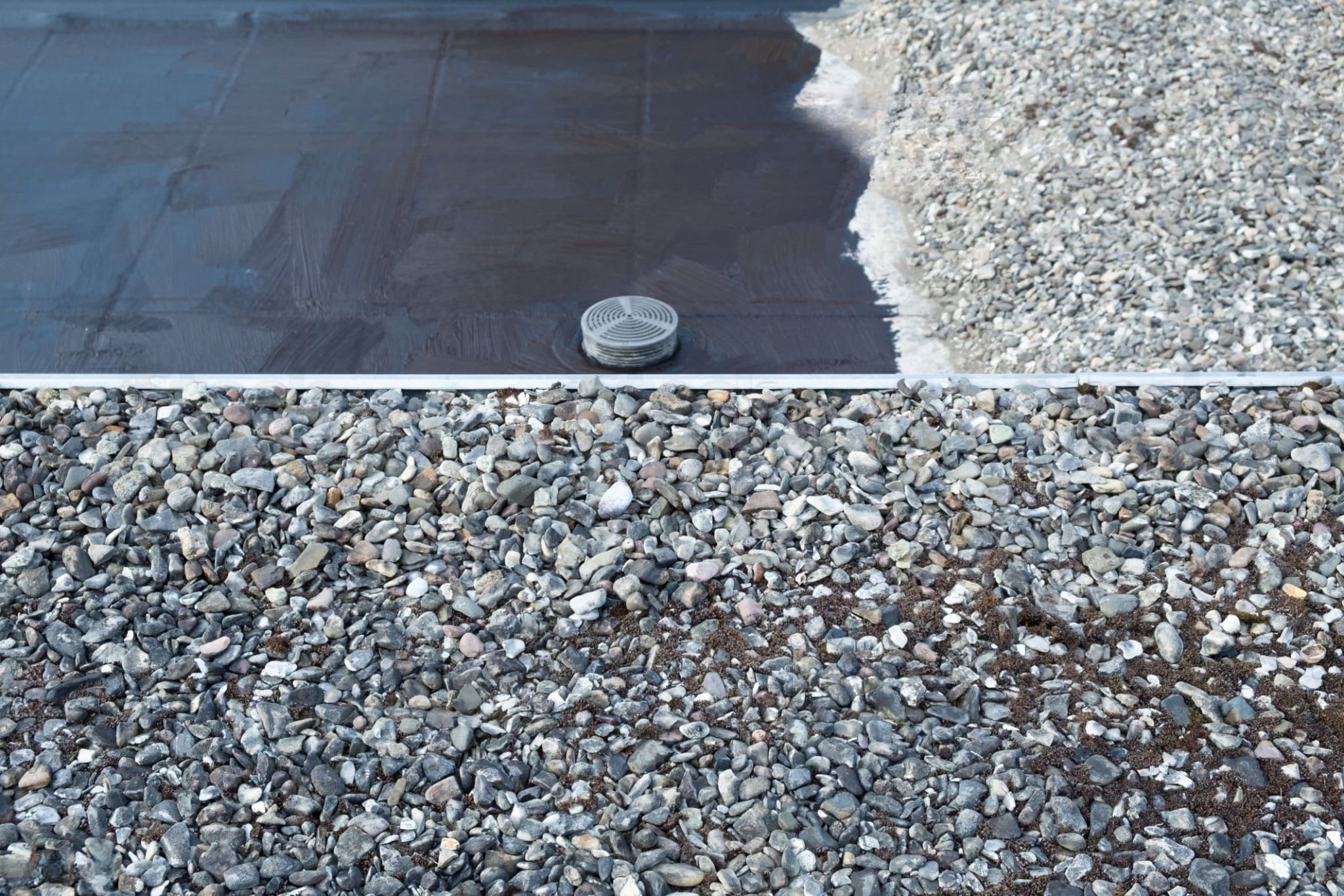 Roof replacement in Quebec showing a flat roof partially covered with gravel, which protects the waterproof membrane from UV rays and damage. A roof drain is visible for rainwater runoff, highlighting the protective and insulating function of gravel on flat roofs.