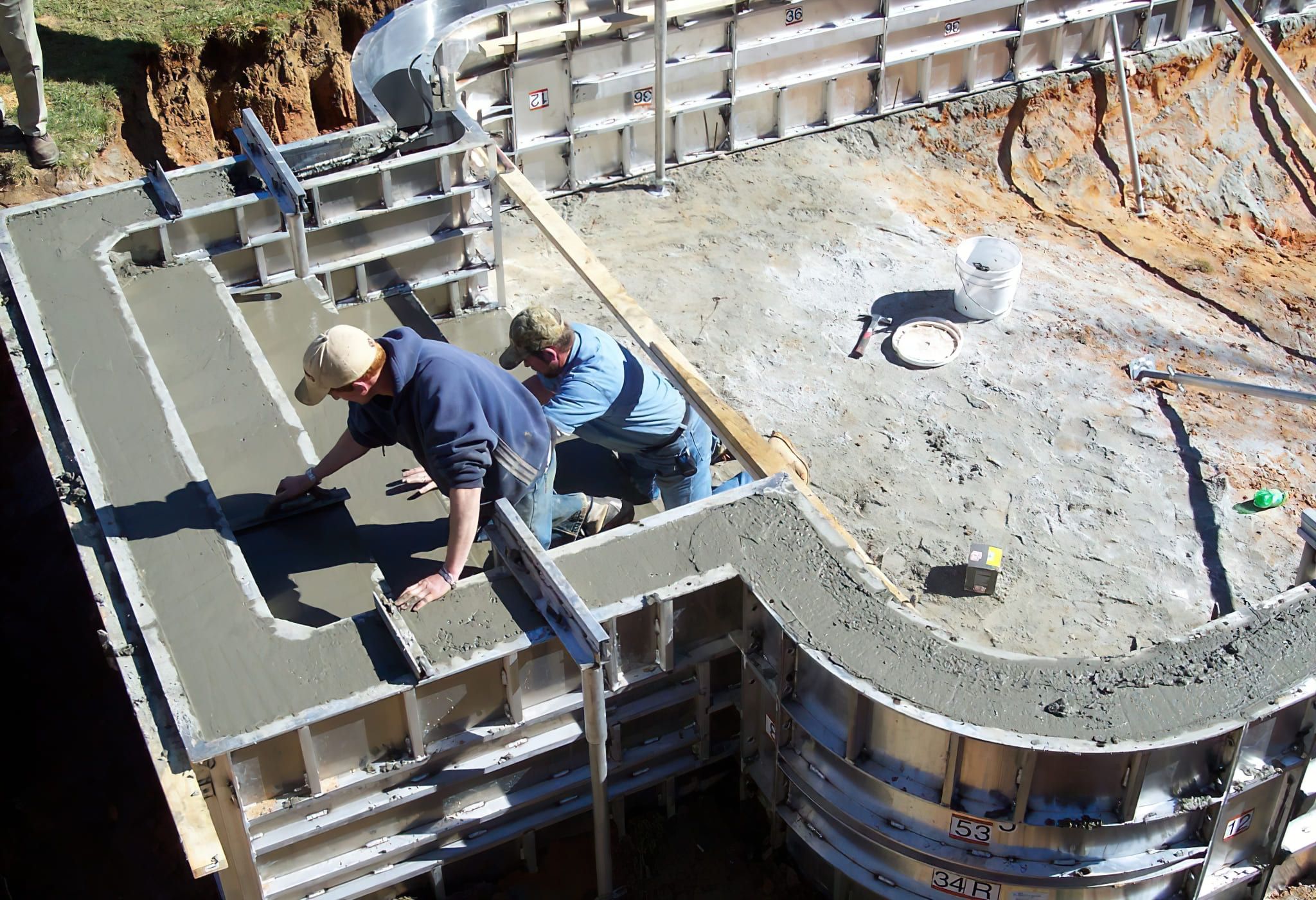 Swimming Pool Installation Quebec and Montreal — construction workers building concrete pool walls using metal formwork to shape the curved structure, ensuring a stable and durable swimming pool foundation.
