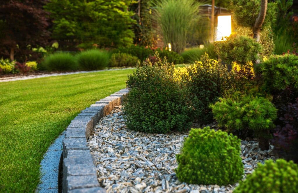 Stone-bordered garden bed with flowers and plants separating it from a green lawn, illustrating professional landscaping services in Quebec.