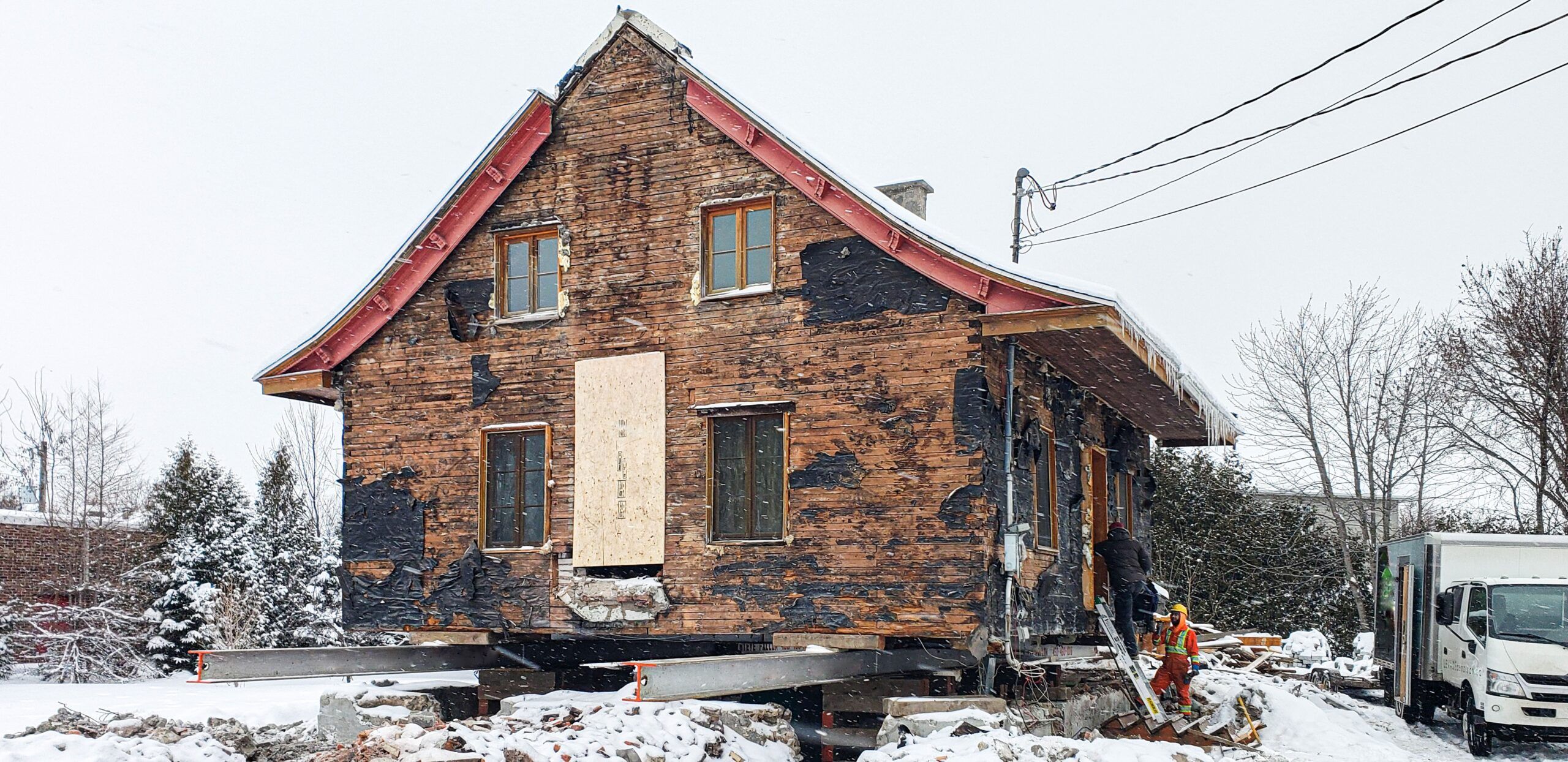 House lifting and relocation in Quebec showing a building raised on a steel frame for transport to a new site, part of a preservation project using specialized equipment during winter conditions to minimize ground impact.